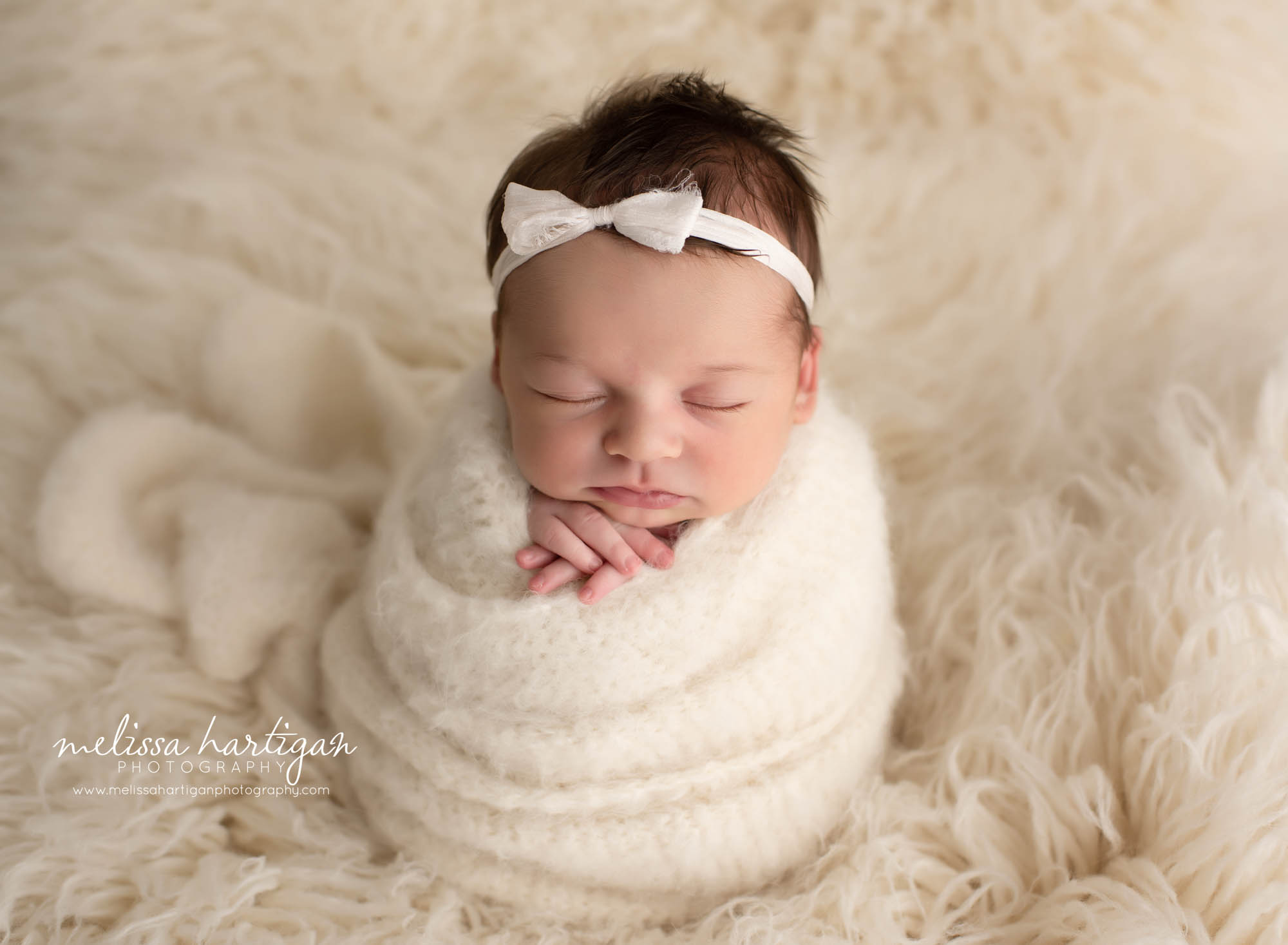 baby girl wrapped in cream wrap on cream flokati with cream bow