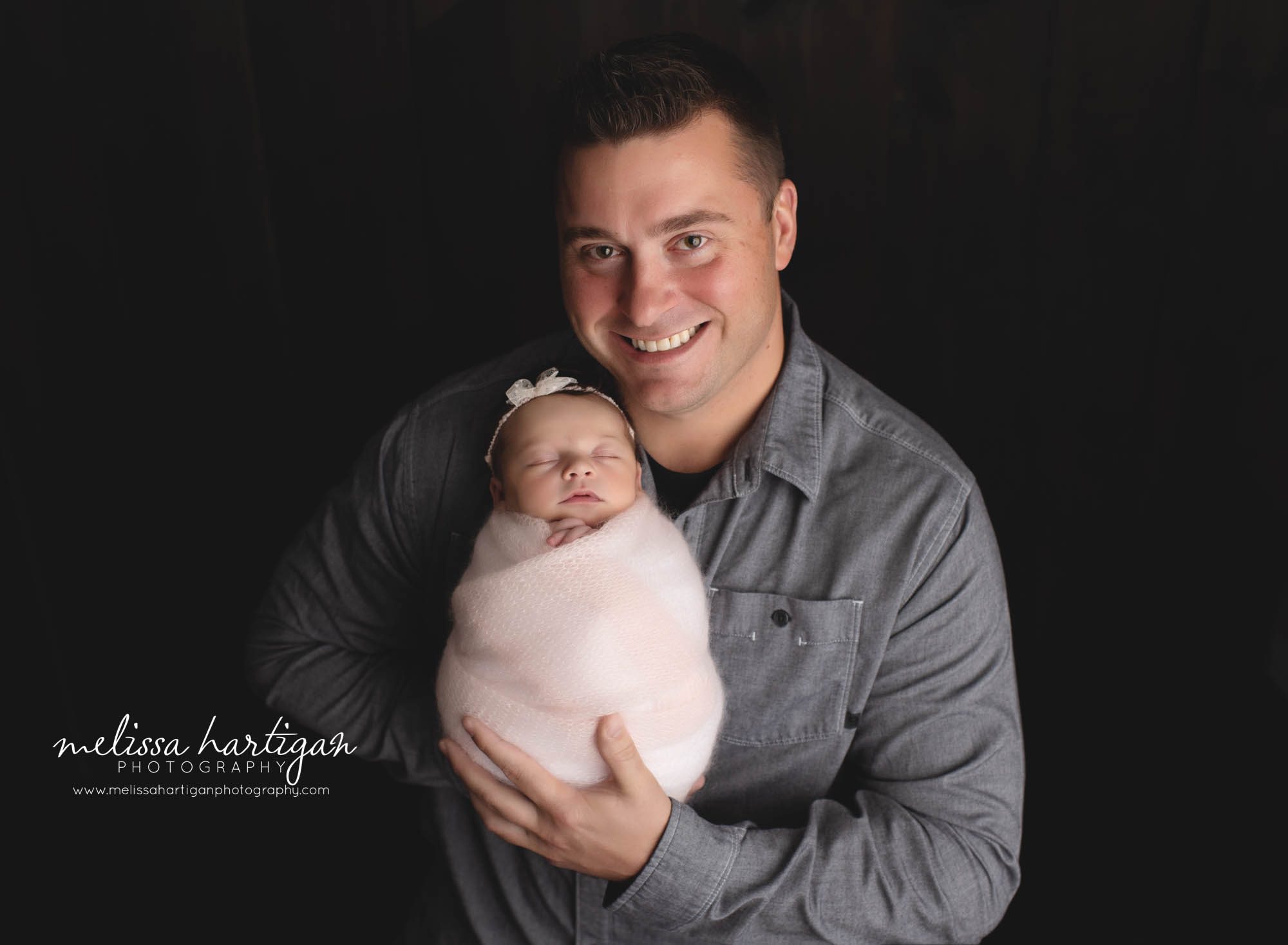 dad holding newborn baby girl wrapped in light pink wrap