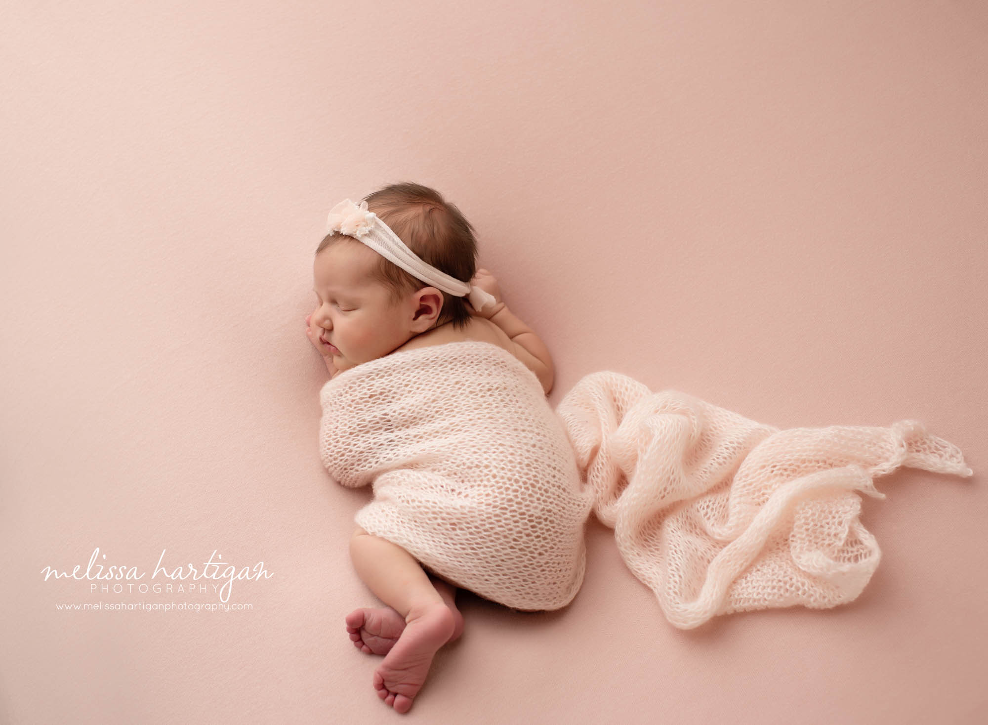 newborn baby girl sleeping on side tummy draped with blush pink knitted wrap and pink headband
