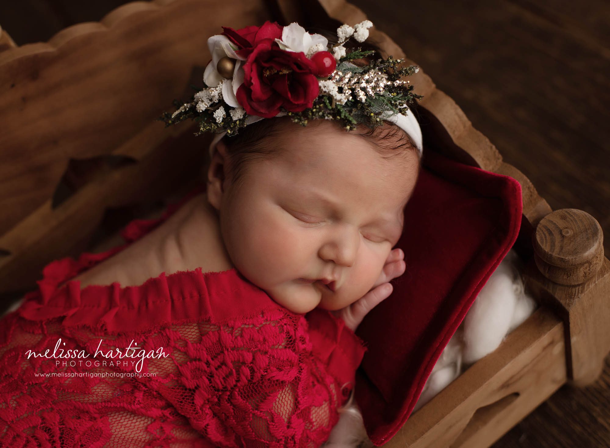 baby girl posed in wooden bed prop with red lace newborn romper and red green and white headband in holiday set up Tolland CT newborn photographer
