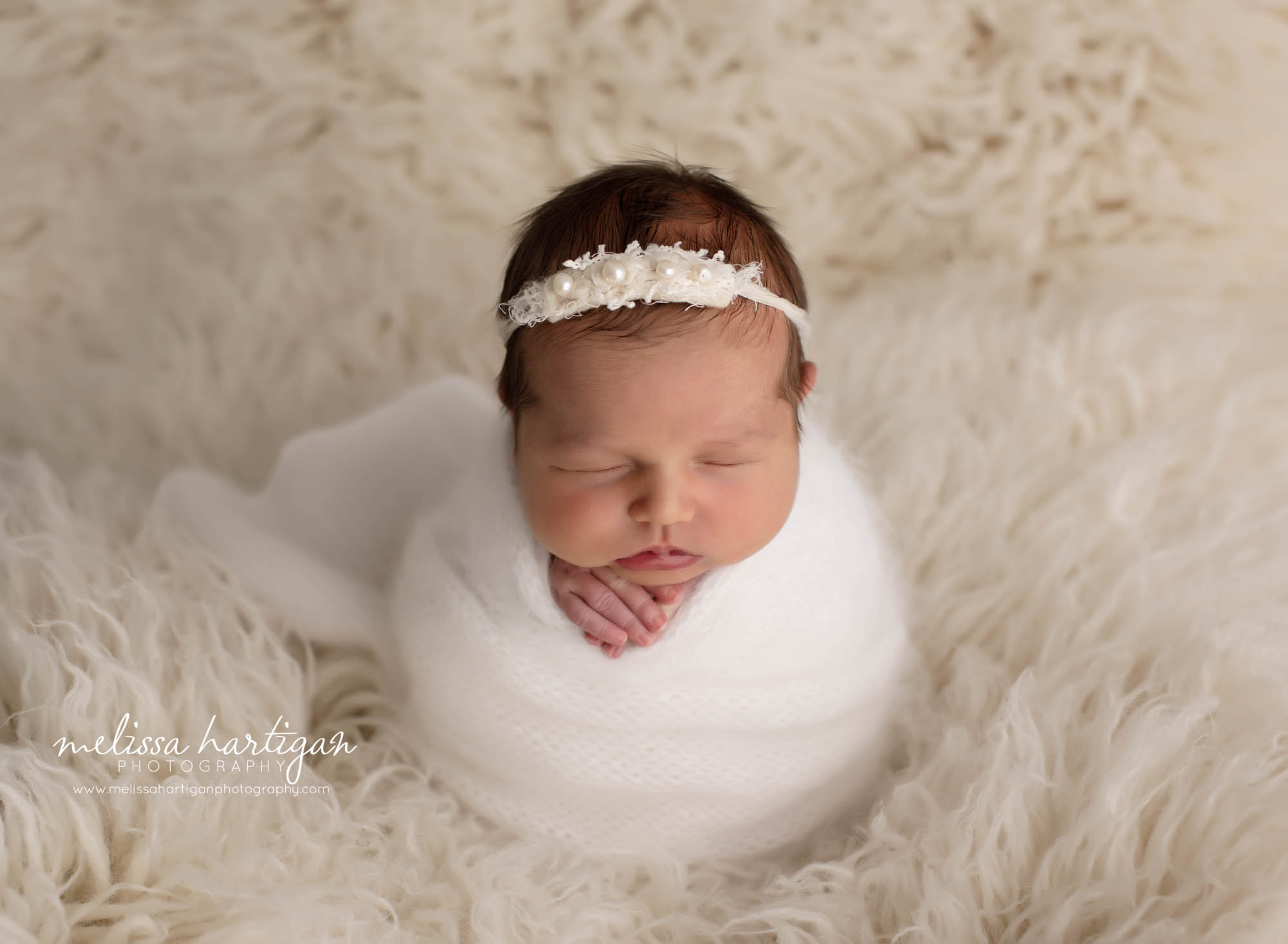 baby girl wrapped in white knitted wrap and white pearl headband