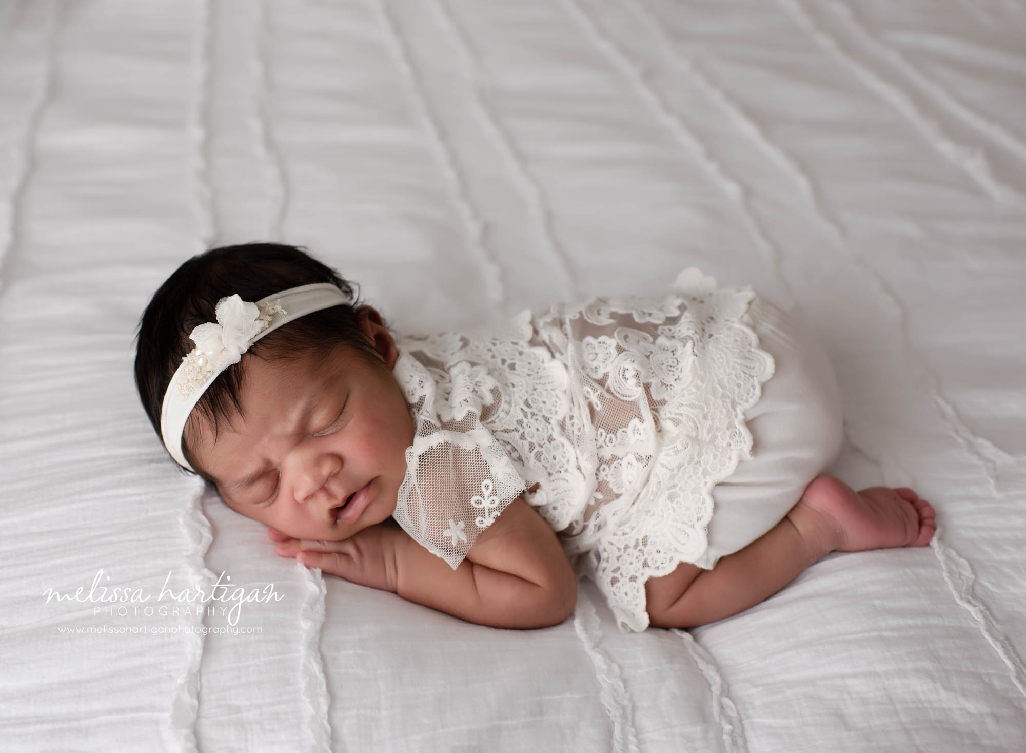 baby girl posed on white bed wearing lacey cream outfit and headband