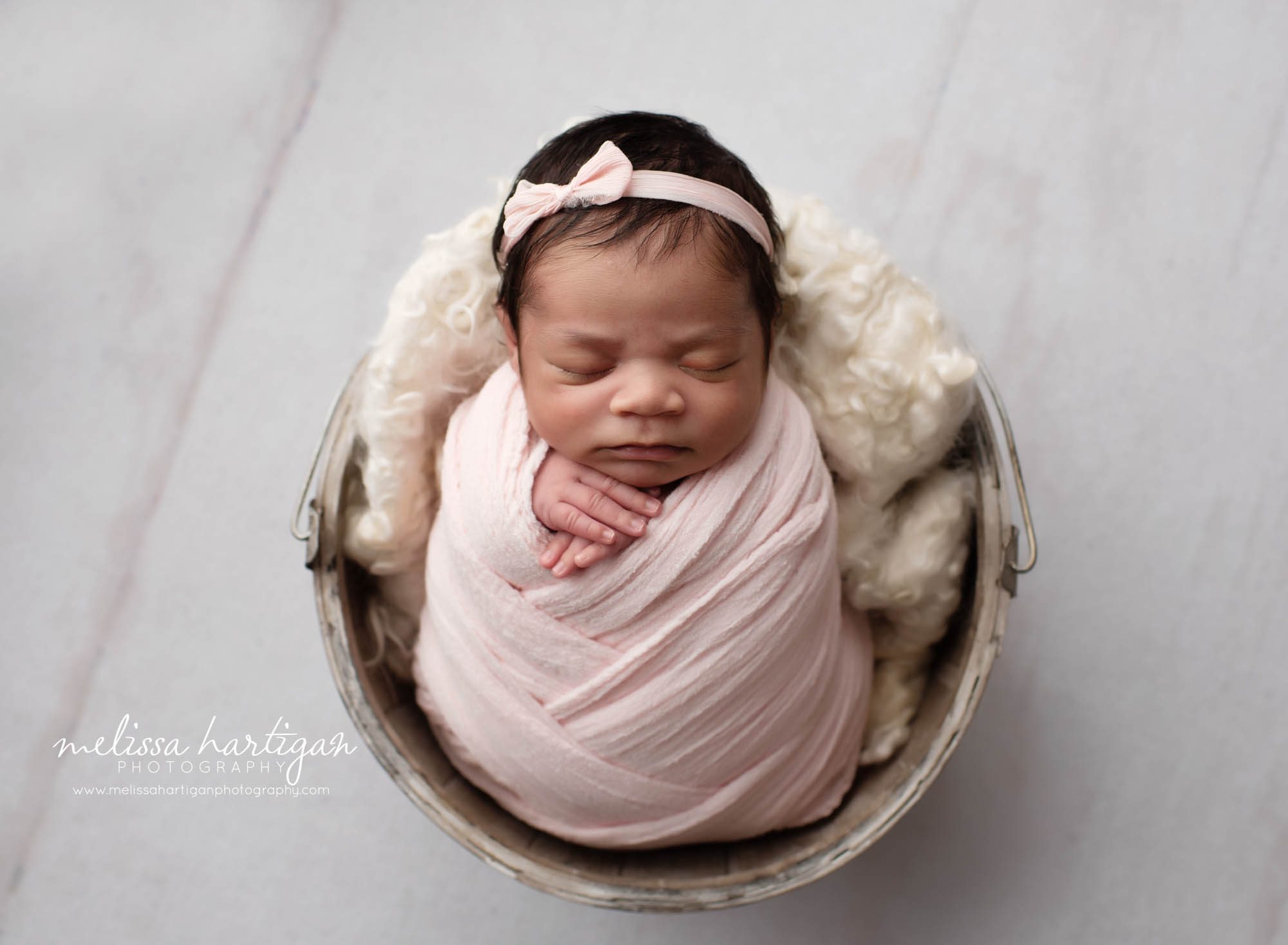 Baby girl wrapped in pink wrap with matching headband posed in bucket