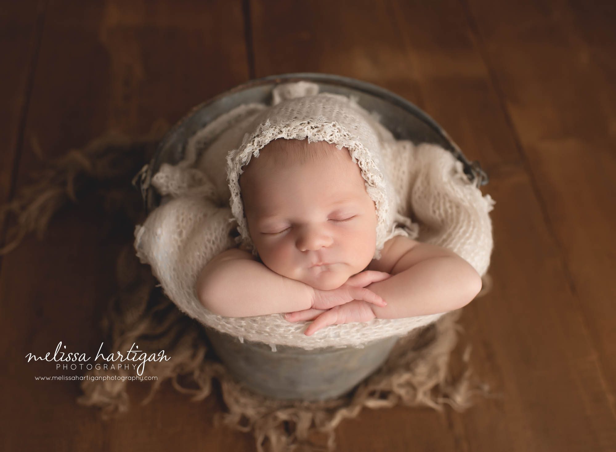 newborn baby girl posed in bucket with cream bonnet