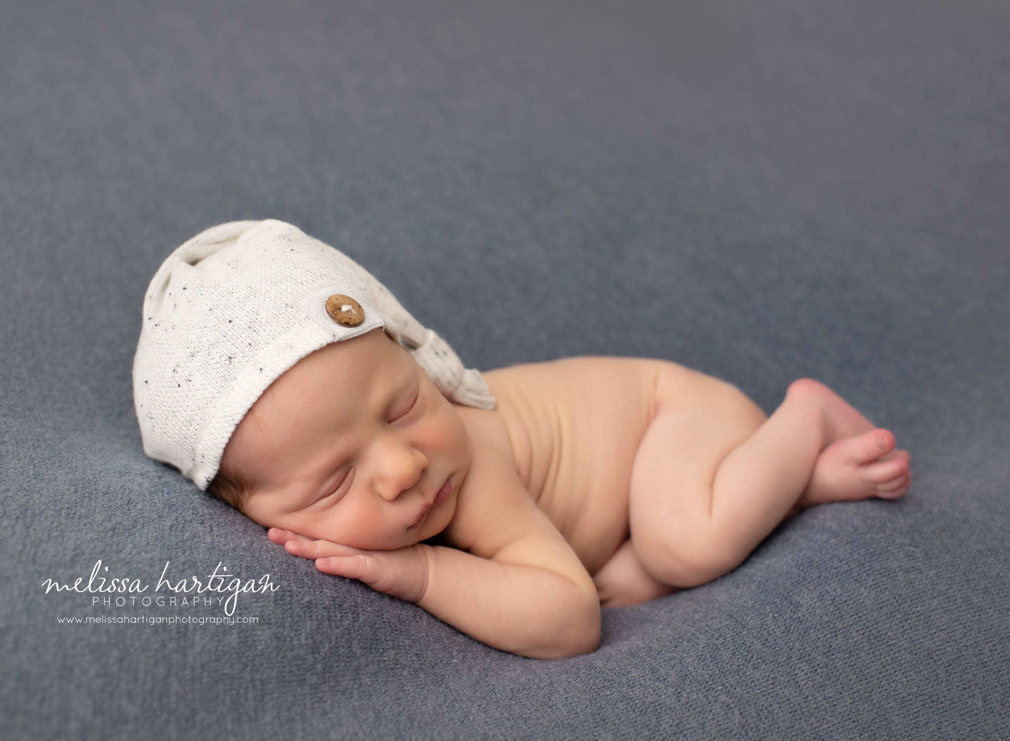 newborn baby boy posed on side wearing cream sleepy cap