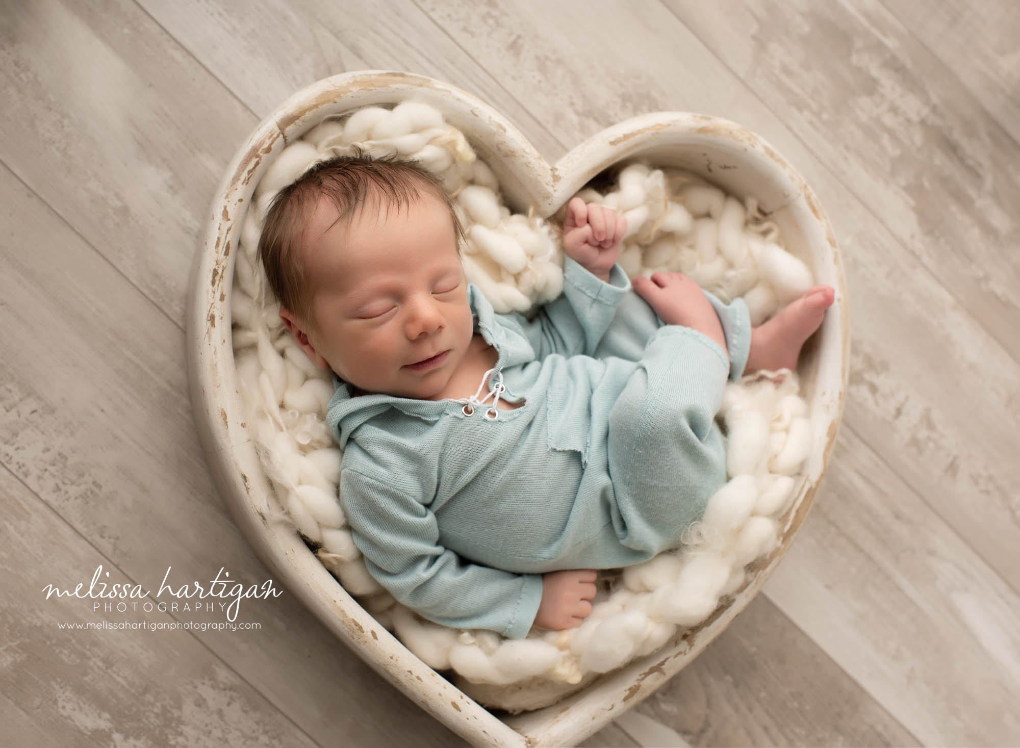 newborn baby boy pose din wooden heart prop with light greenish blue outfit