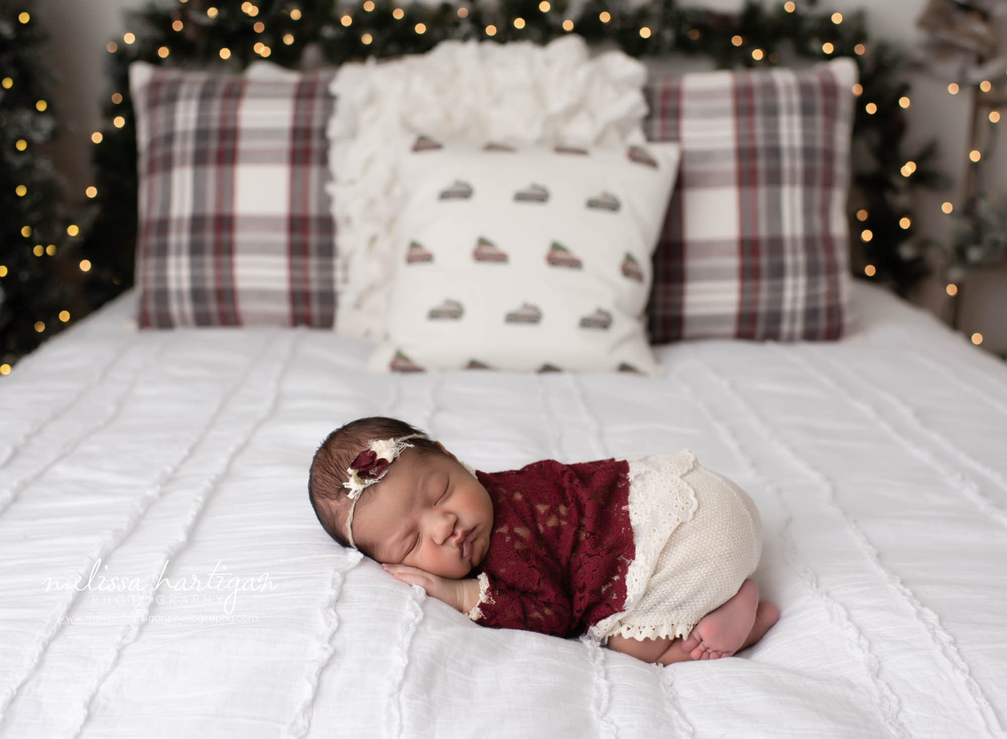 Newborn baby girl posed on bed with green garland light with white christmas lights newborn baby holiday birth announcement photo