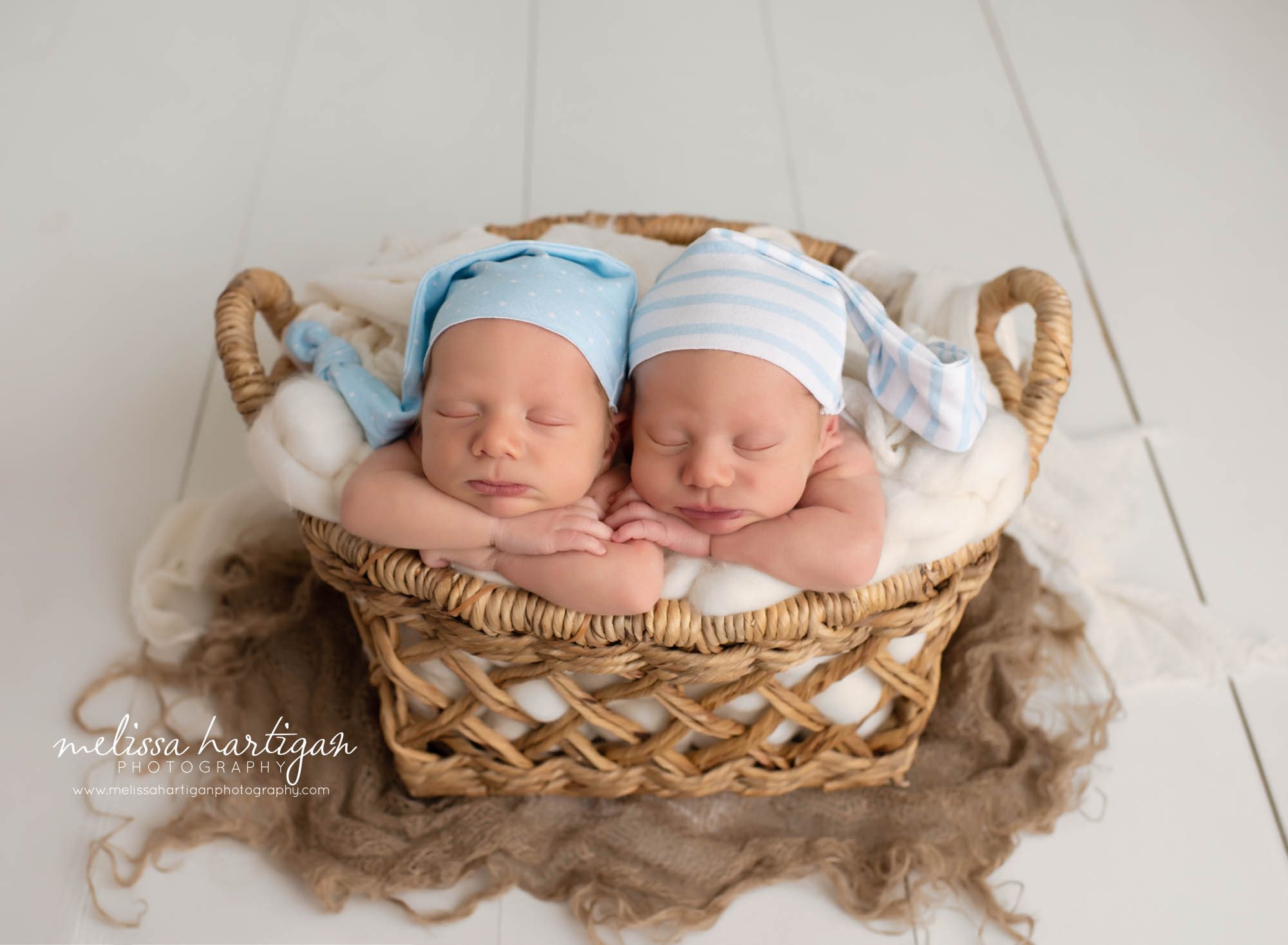 twin newborn boys posed in basket with blue and cream sleepy caps on