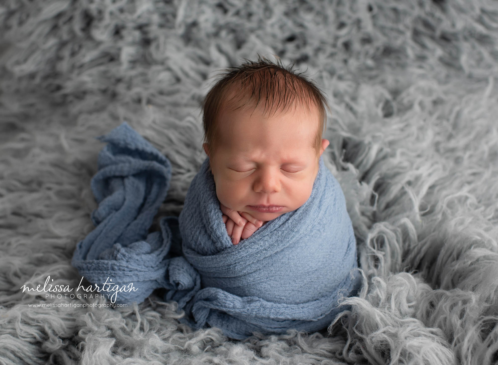 baby boy wrapped in blue wrapp posed on flokati rug newborn photography