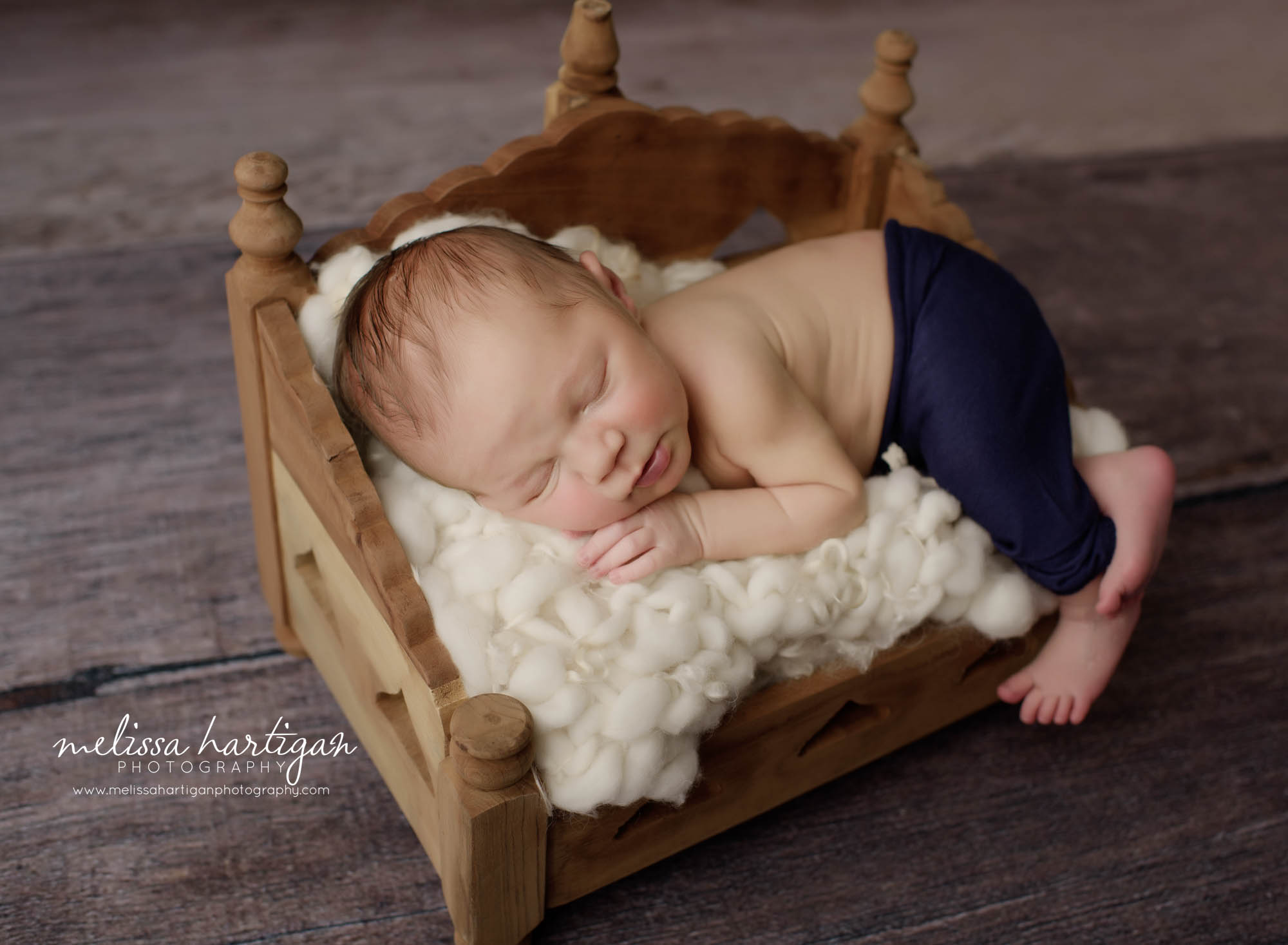 baby boy posed on woodenday bed prop with cream layer and navy blue pants