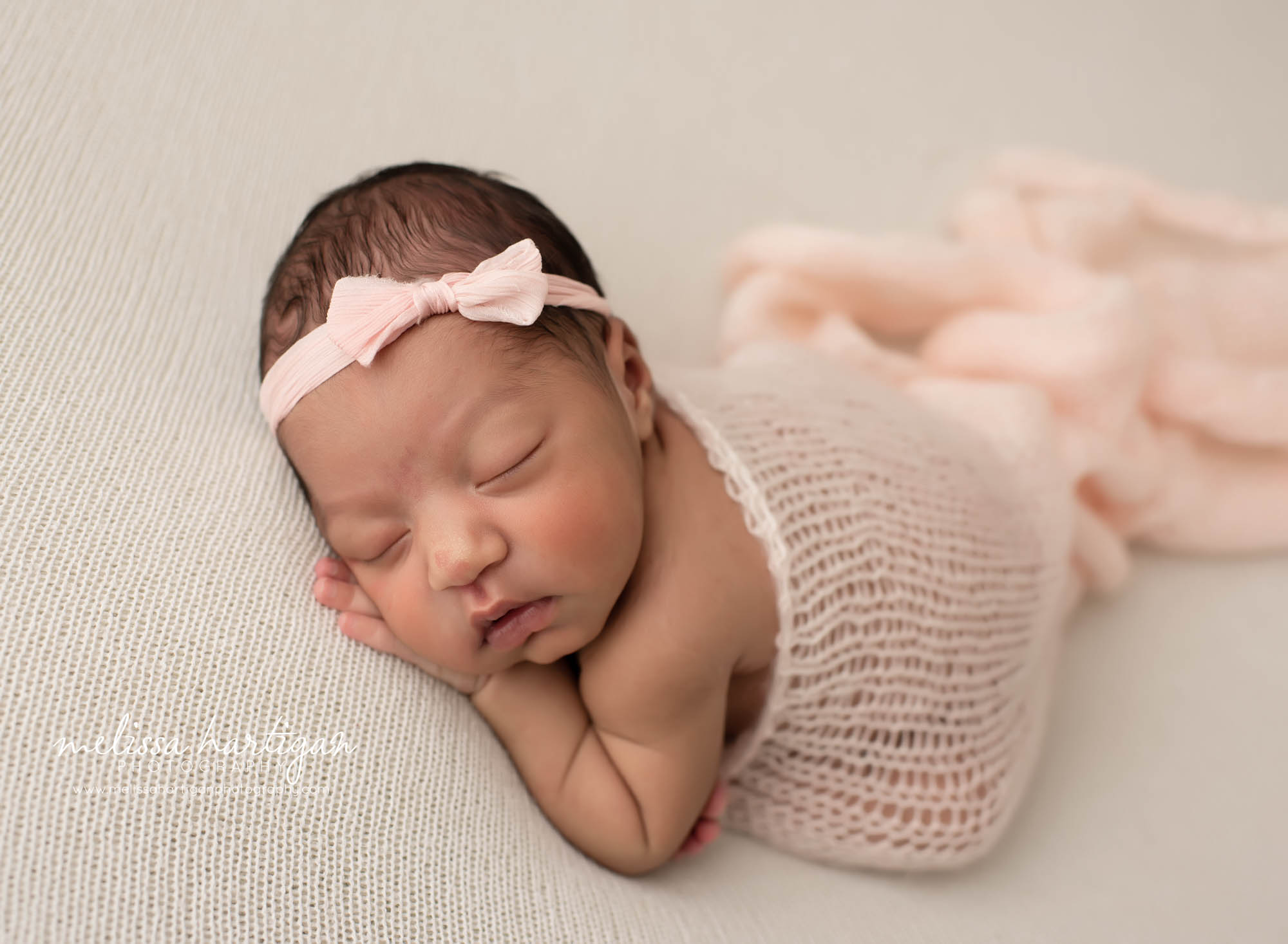 Baby girl posed taco pose with light pink knitted wrap draping baby girl wearing pink bow headband Hartford CT newborn Photography