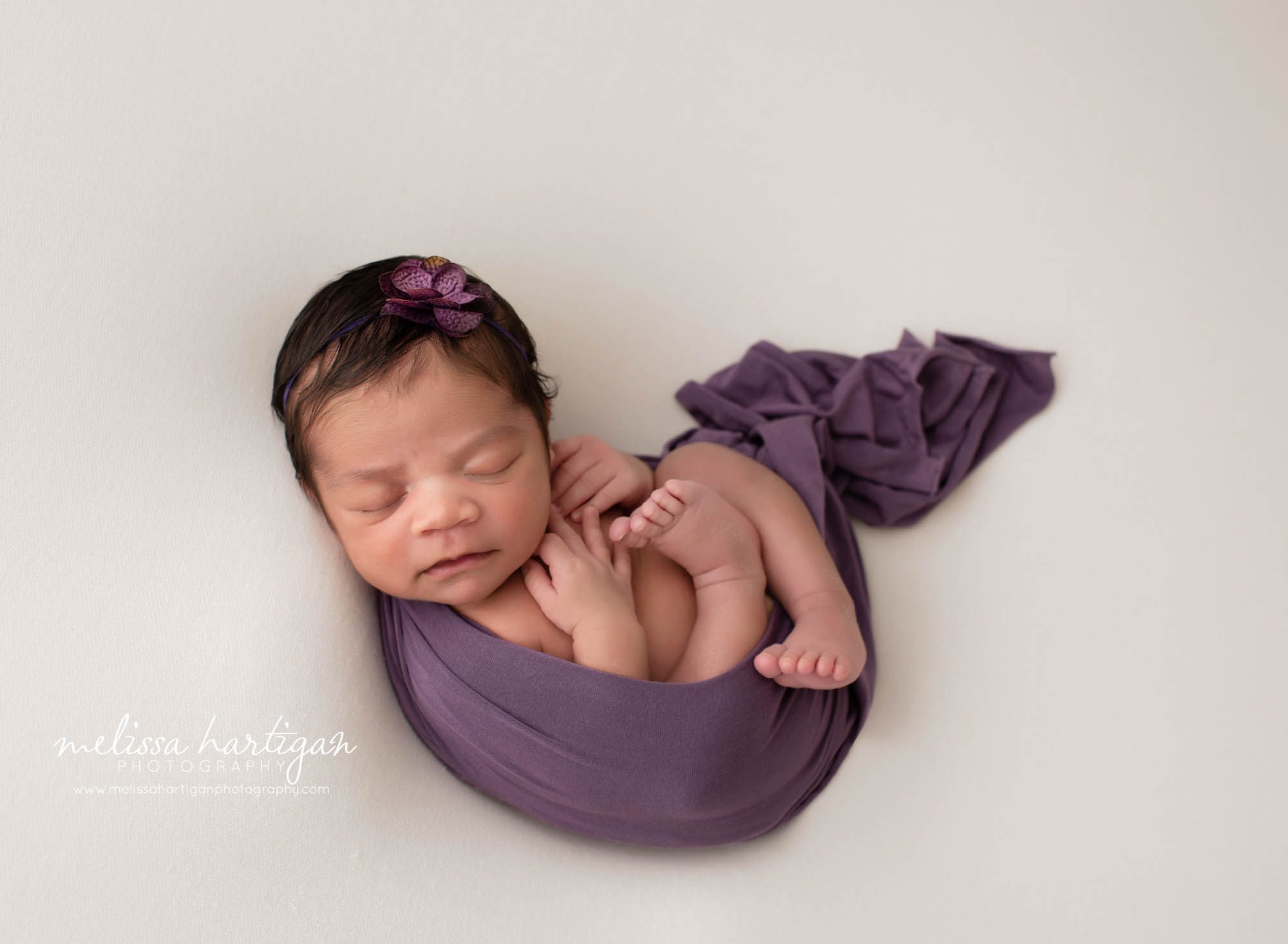 baby girl wrapped in purple wrap with purple headband on