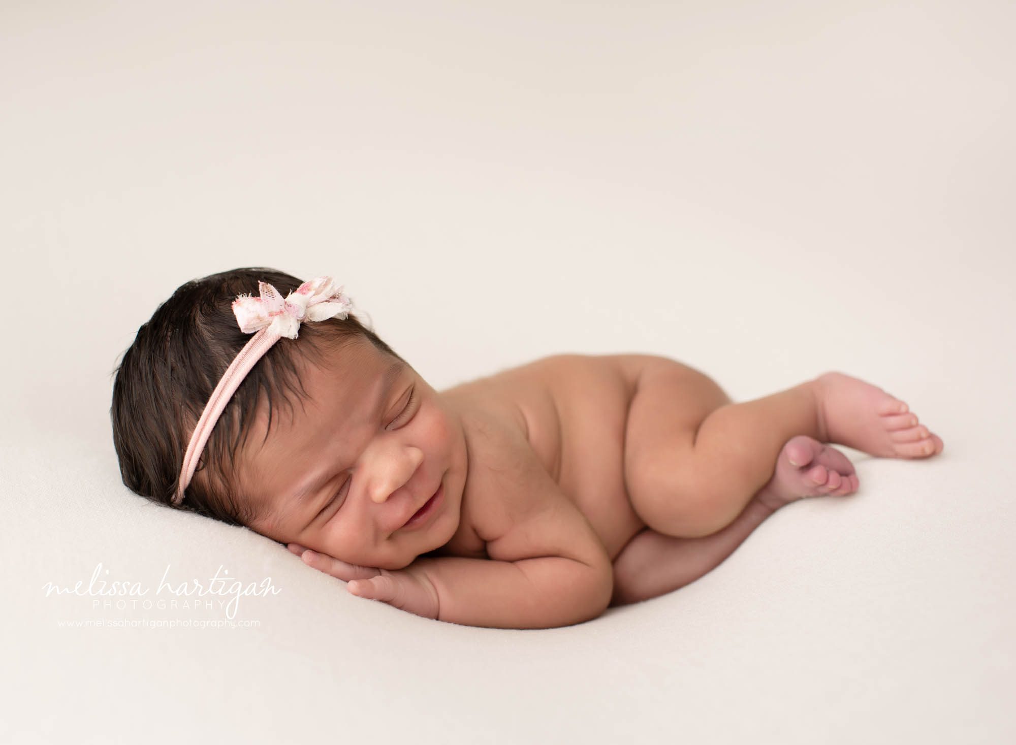 baby girl smiling posed on cream backdrop wearing pink headband CT newborn Photographer
