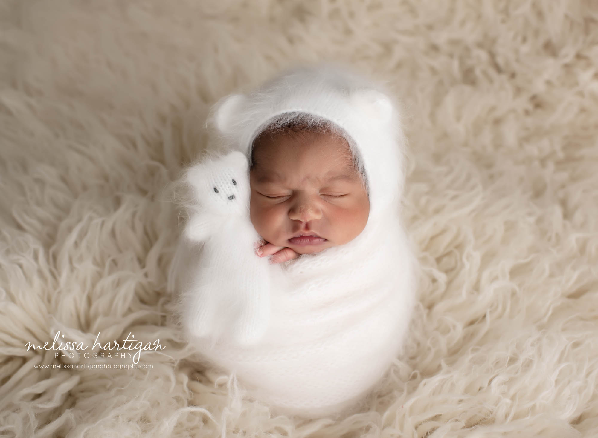 baby girl wrapped in white knitted wrap with matching bear bonnet and matching teddy bear in white
