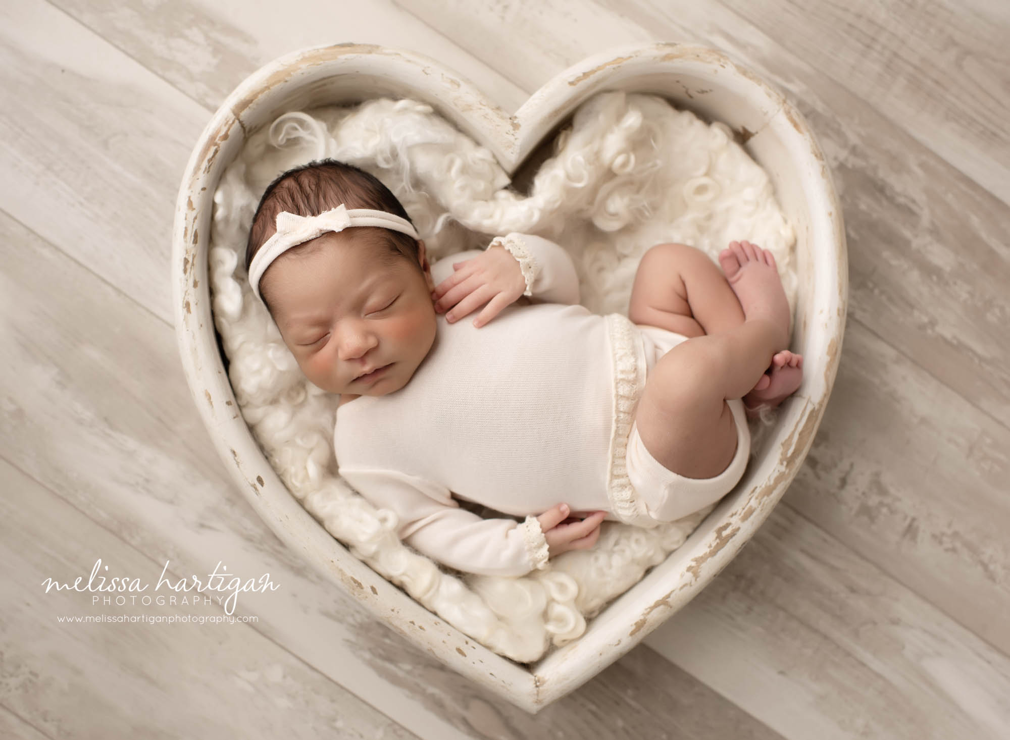 Newborn Bbay girl posed in white wooden heart prop wearing cream cromper and cream bow headband Hartford CT Newborn Photography