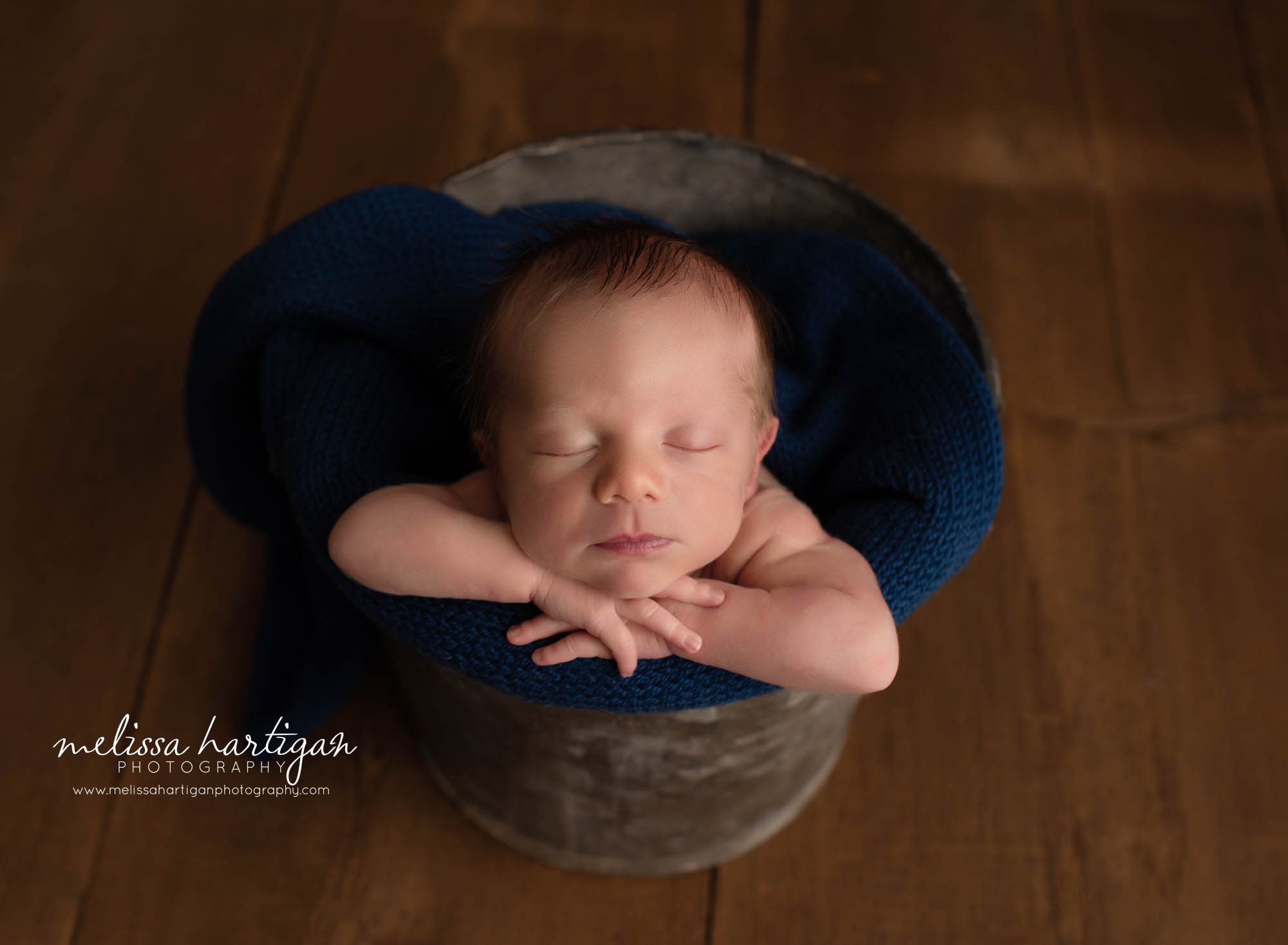 baby boy posed in bucket with chin on hands navy blue knitted wrap