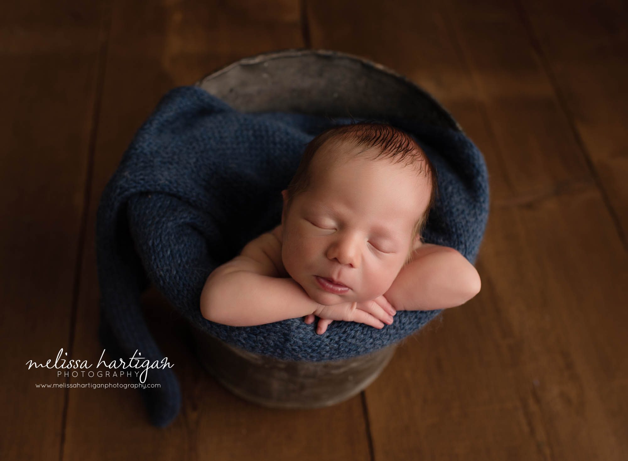 baby boy posed in bucket with chin on hands navy blue knitted wrap