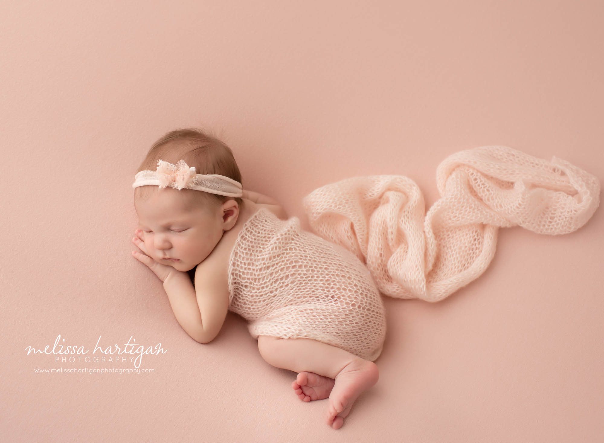 newborn baby girl posed on pink posing fabric with light pink knitted wrap and pink bow headband