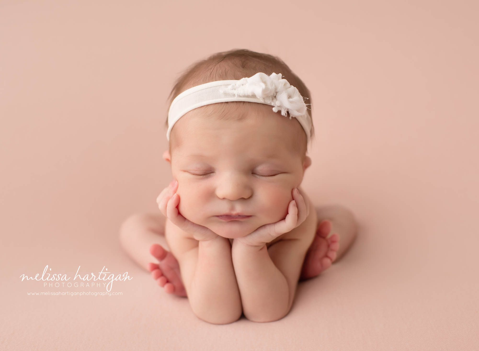 newborn baby girl posed in froggy pose with white headband