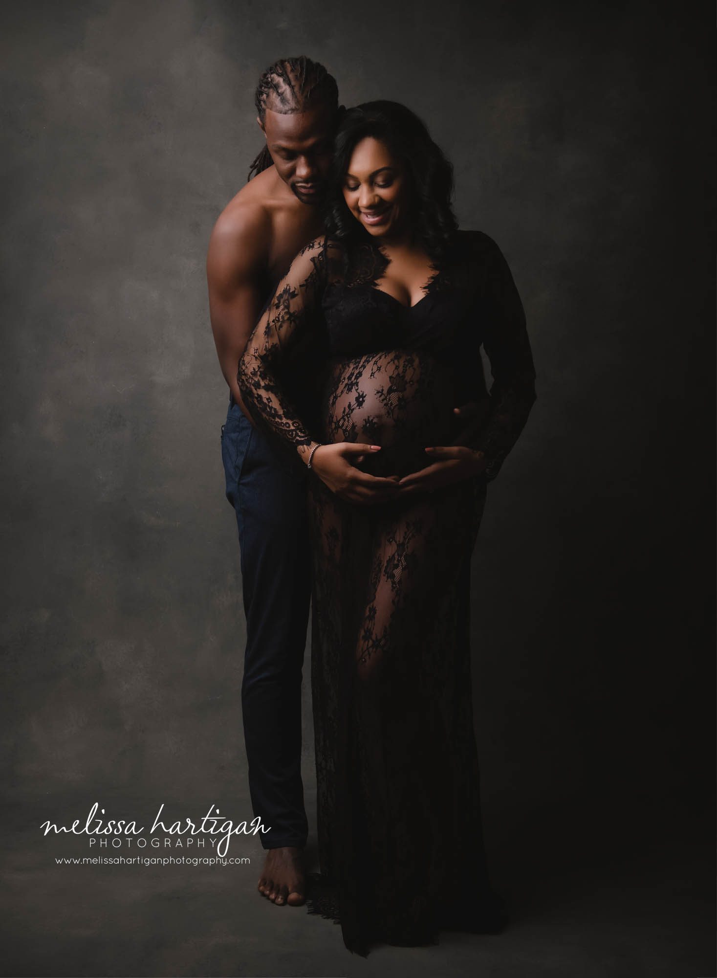 expectant couple holding and looking down at baby bump standing pose studio maternity photography session