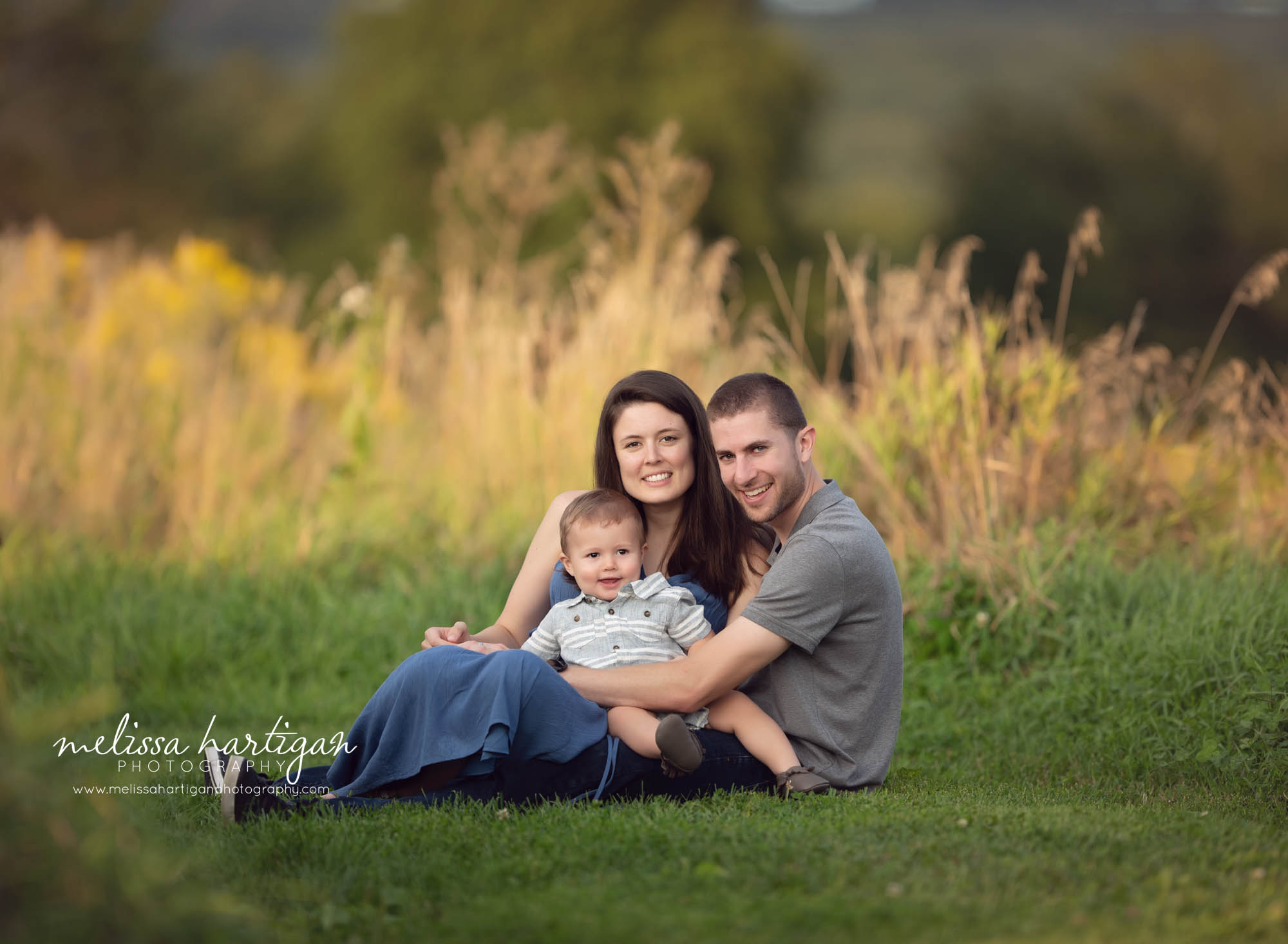 mom dad and toddler boy sitting on grass CT family photography session in park