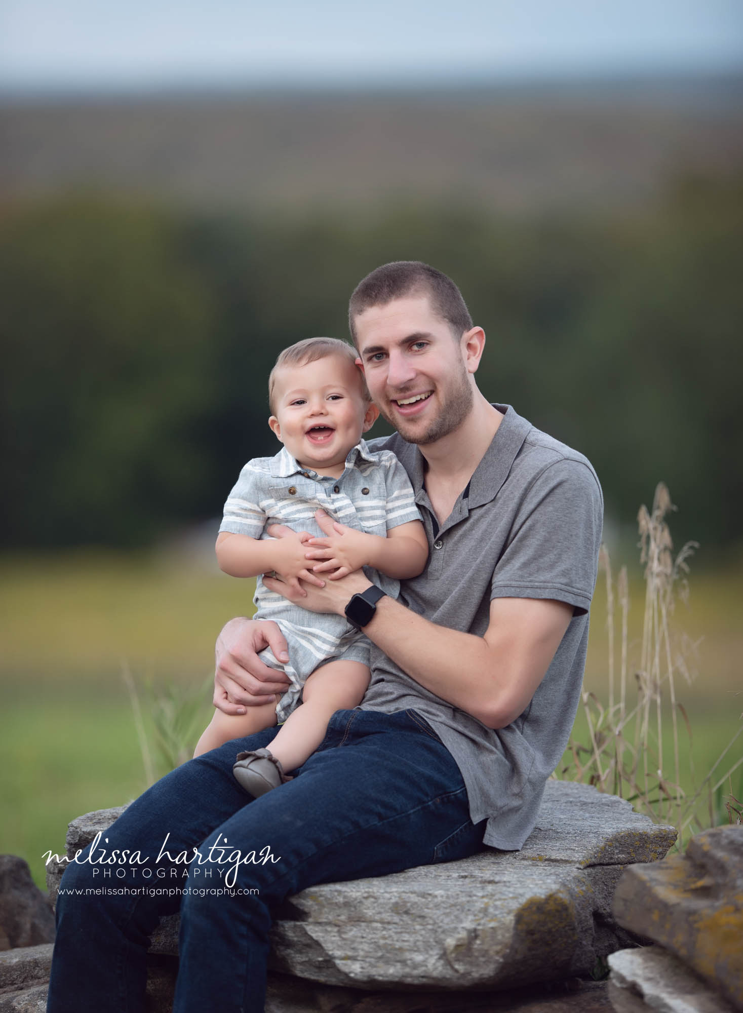 Dad sitting on rock holding smiling toddler son family photographer Connecticut