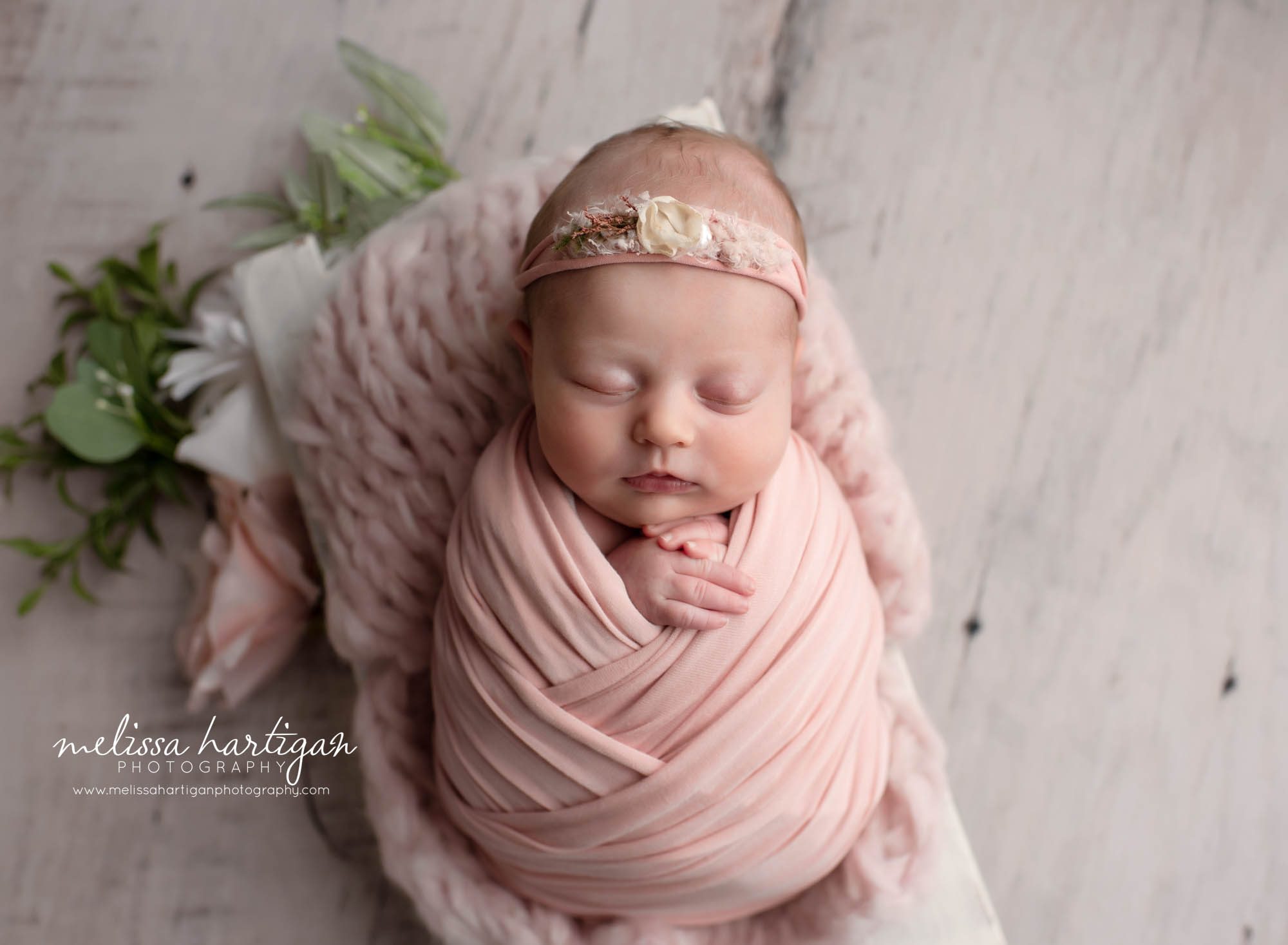newborn baby girl posed in wooden prop swaddled in pink wrap with floral pink headband and floral elements Ct newborn photographer
