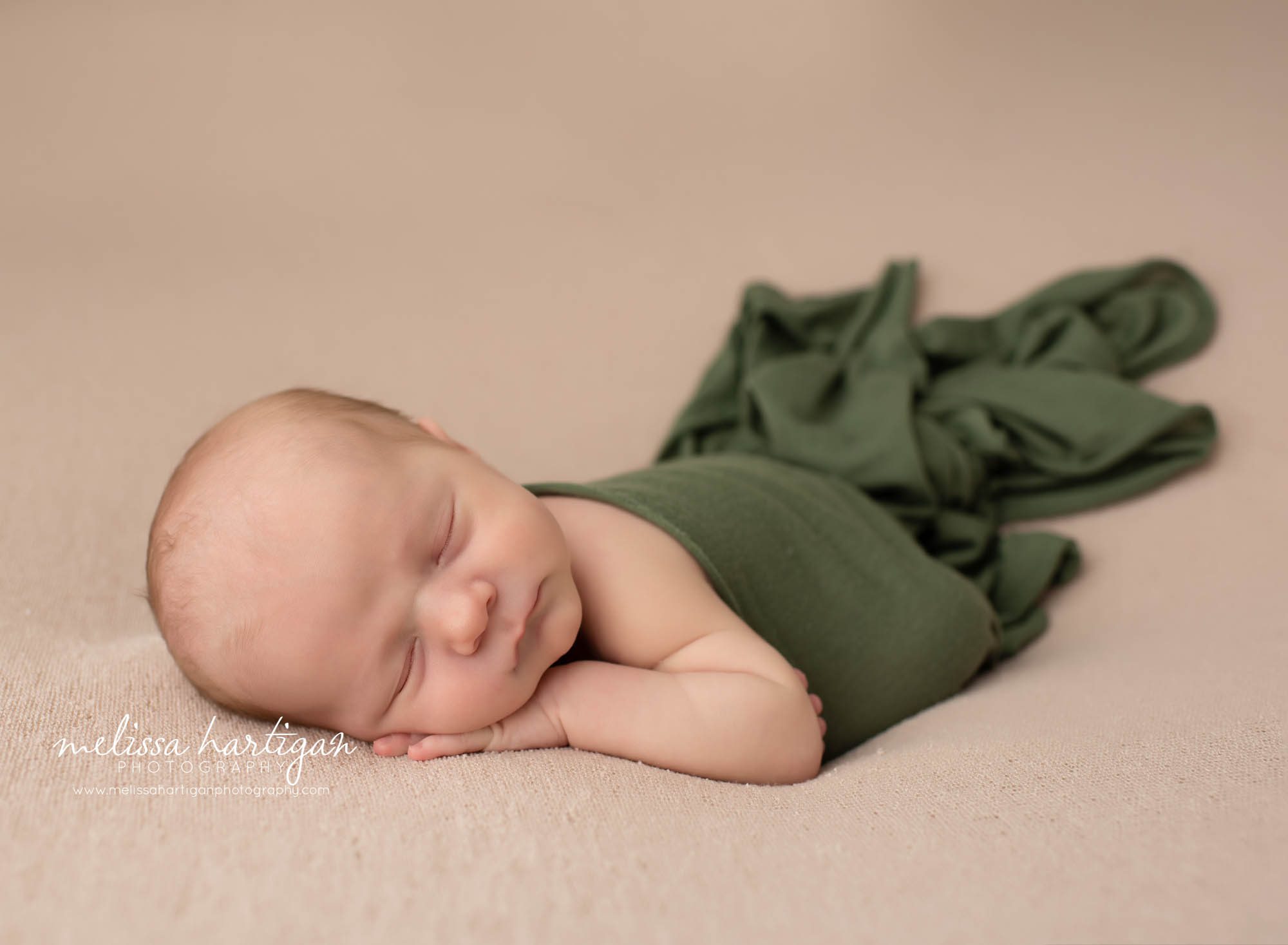 newborn baby boy posed on tummy with hand under cheek green wrap draped over baby