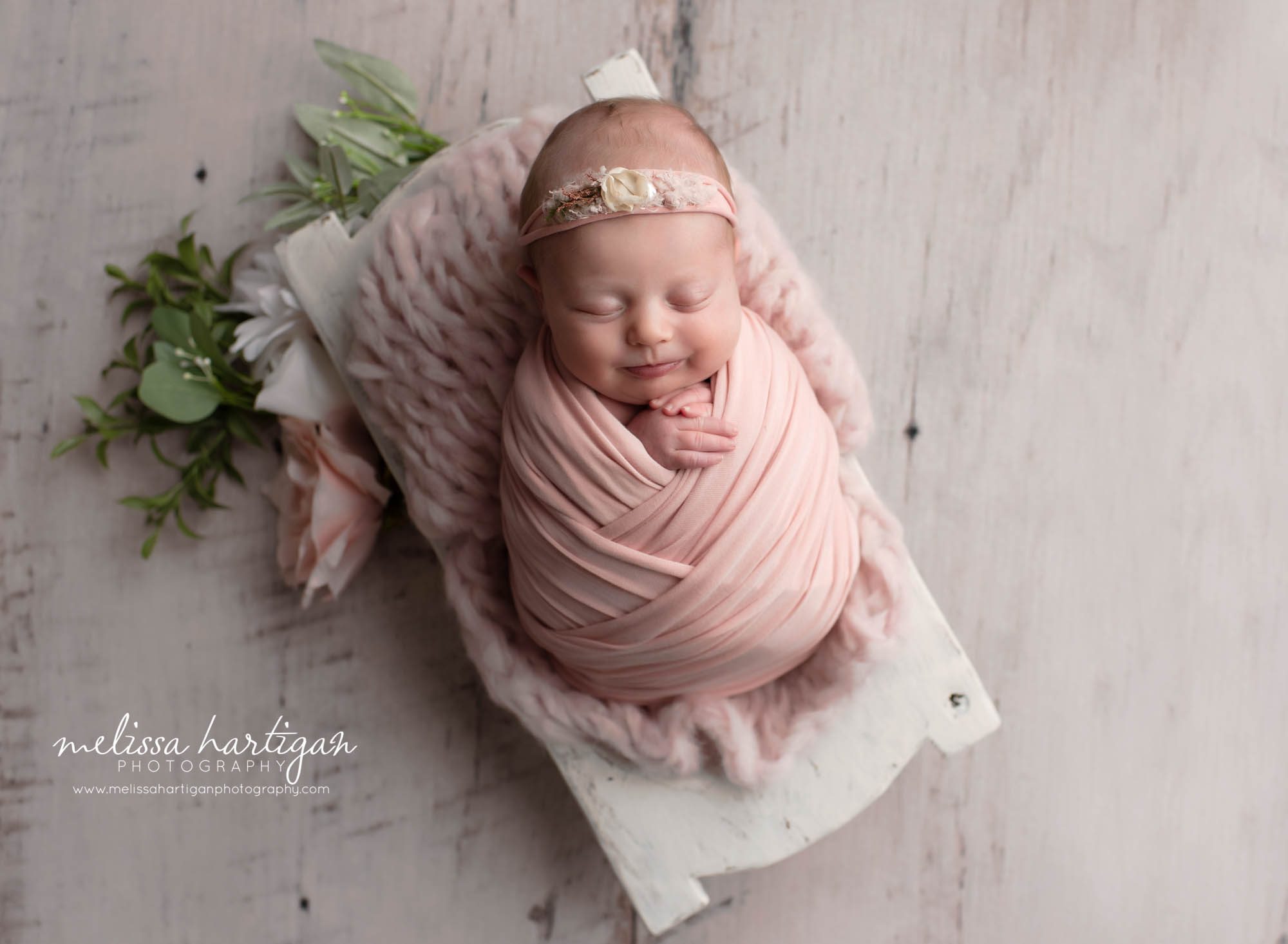 baby girl wrapped in pink wrap, pink knitted layer, pink floral headband and floral elements around wooden prop coventry ct newborn photography