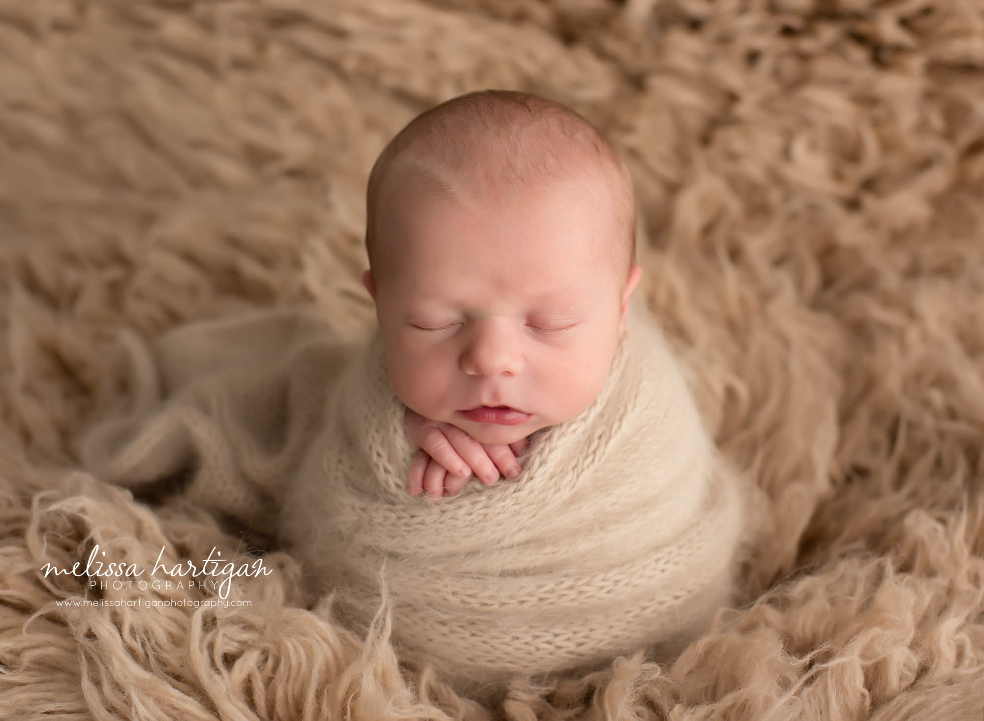 newborn baby boy posed on flokati rug light caramel color with tan knitted wrap