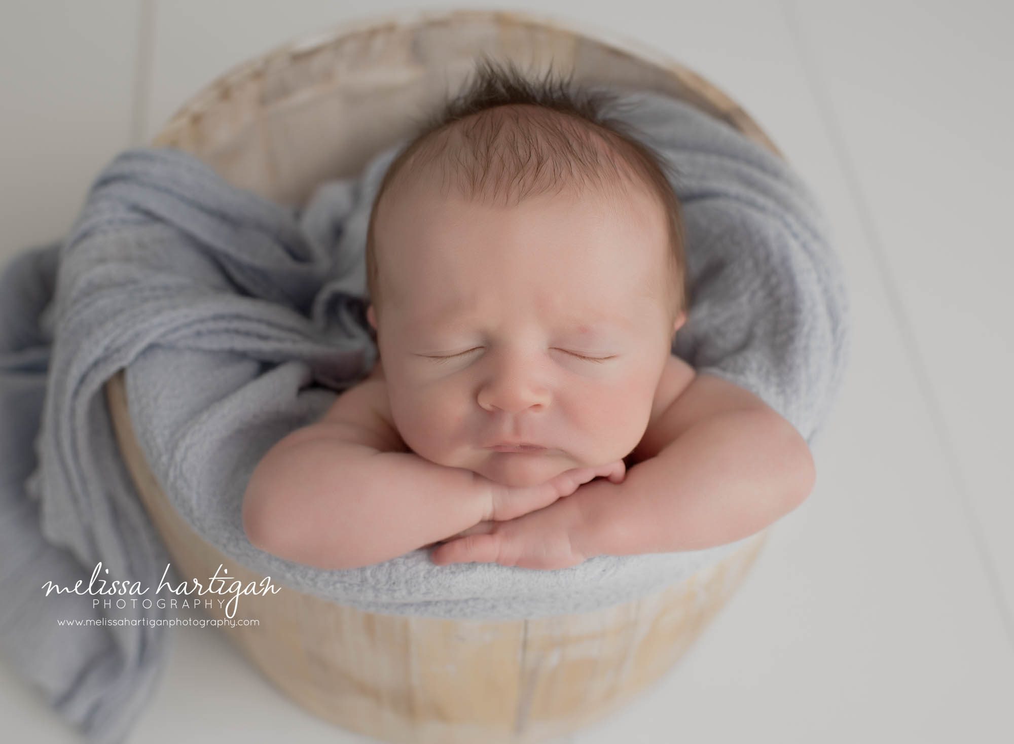 newborn boy posed in wooden bucket with light gray sleepy cap with stripes Tolland Newborn Photography