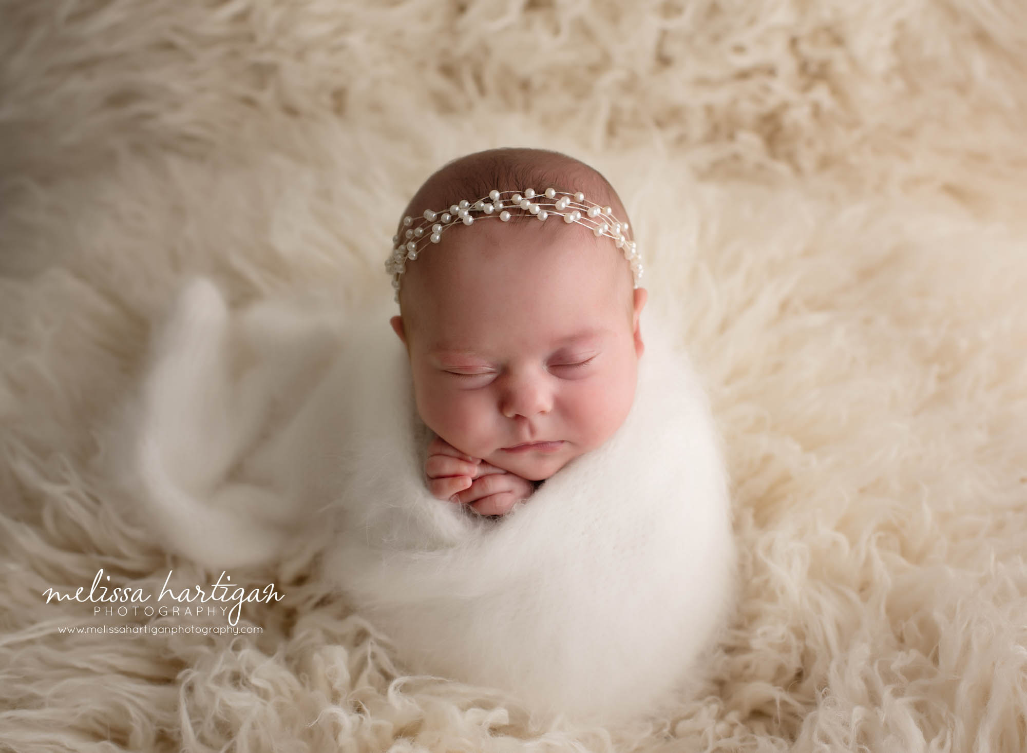 newborn baby girl wrapped and posed on cream flokati