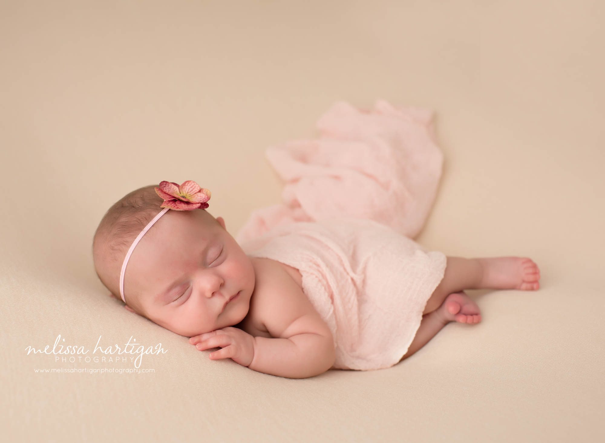 newborn baby girl posed on side with floral headband and knitted layer wrap