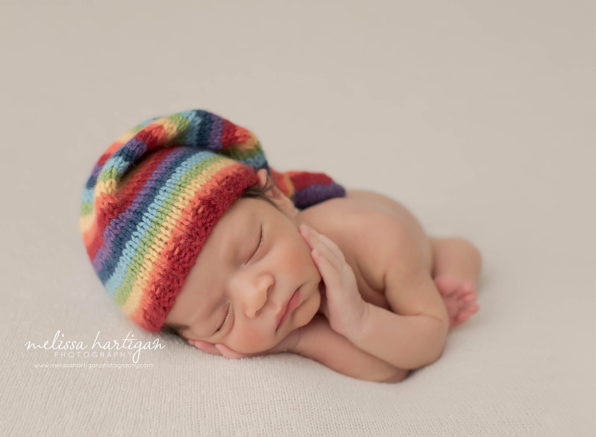 Newborn baby boy posed on side wearing knitted rainbow baby sleepy cap