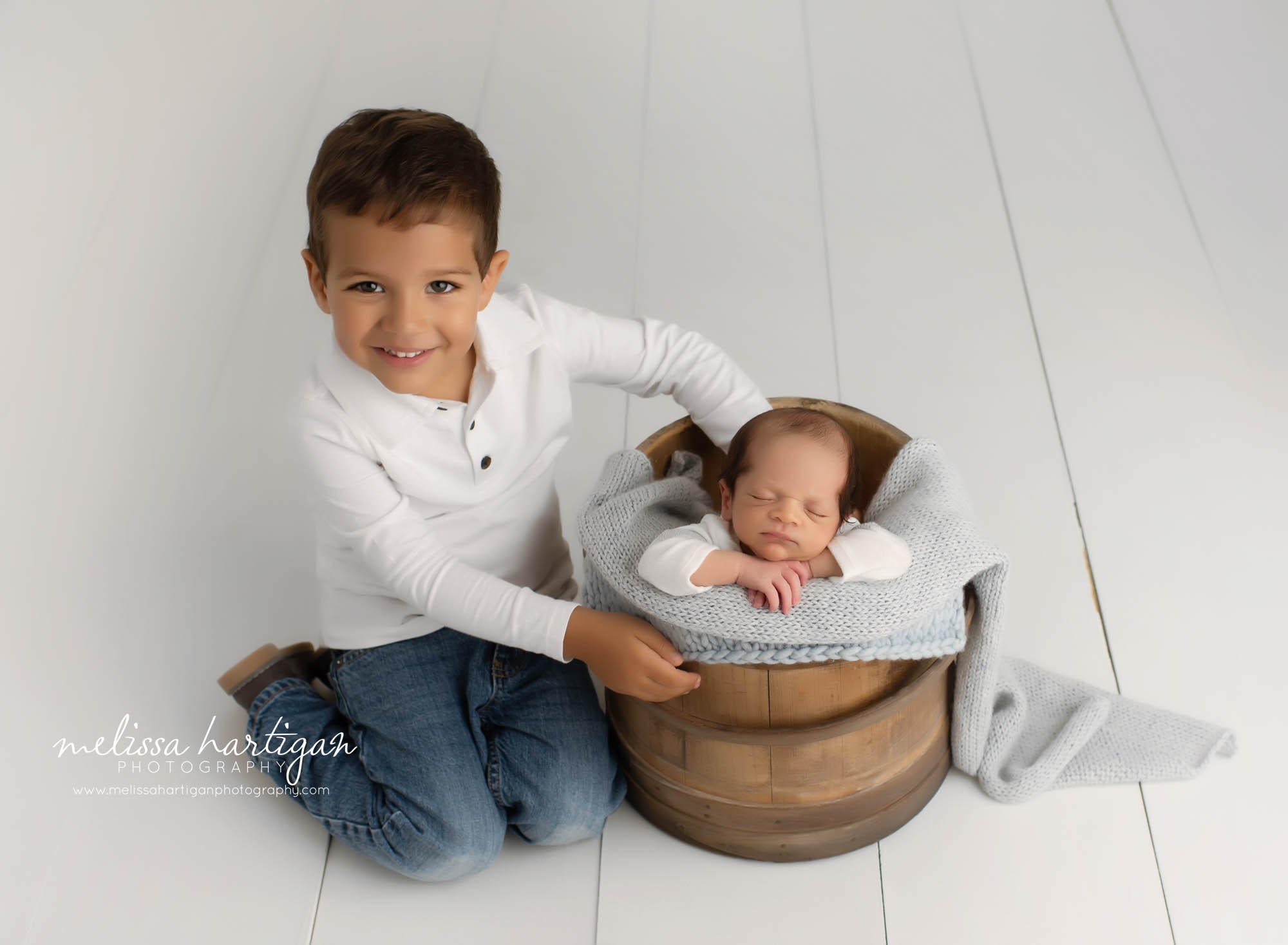 newborn baby boy posed in wooden bucket big brother sitting beside smiling