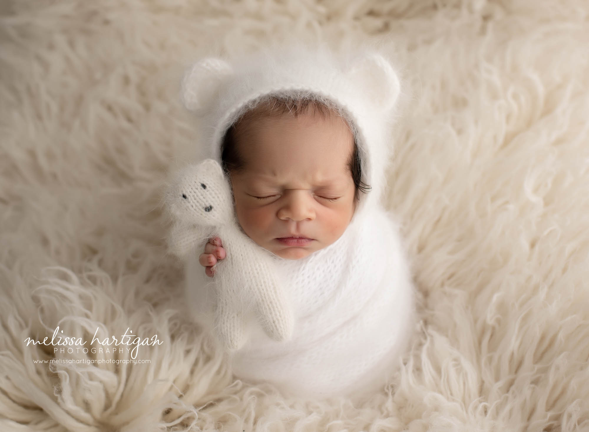 Newborn baby boy wrapped in white knitted wrap with matching teddy bear and bear bonnet