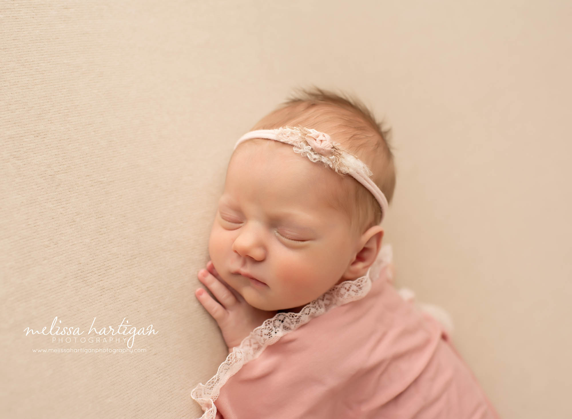 newborn baby girl posed on side with pink lace wrap draped over and pink flower headband