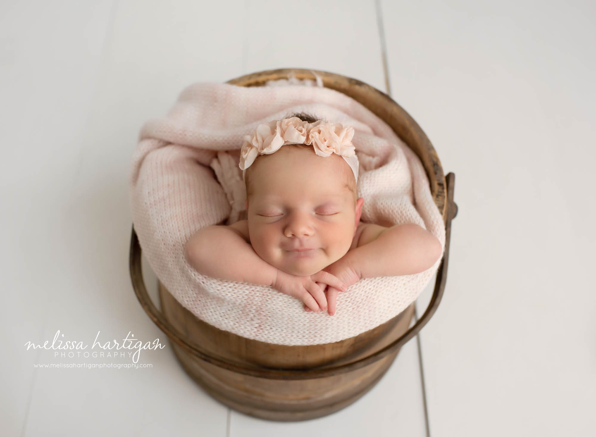 newborn baby girl posed in wooden bucket with light pink knitted wrap layer and flower headband Hamden CT newborn Photography