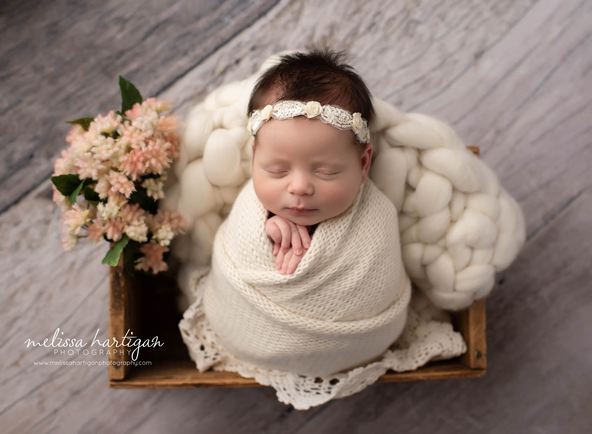 Newborn baby girl wrapped in cream wrap in wooden box with flower elements