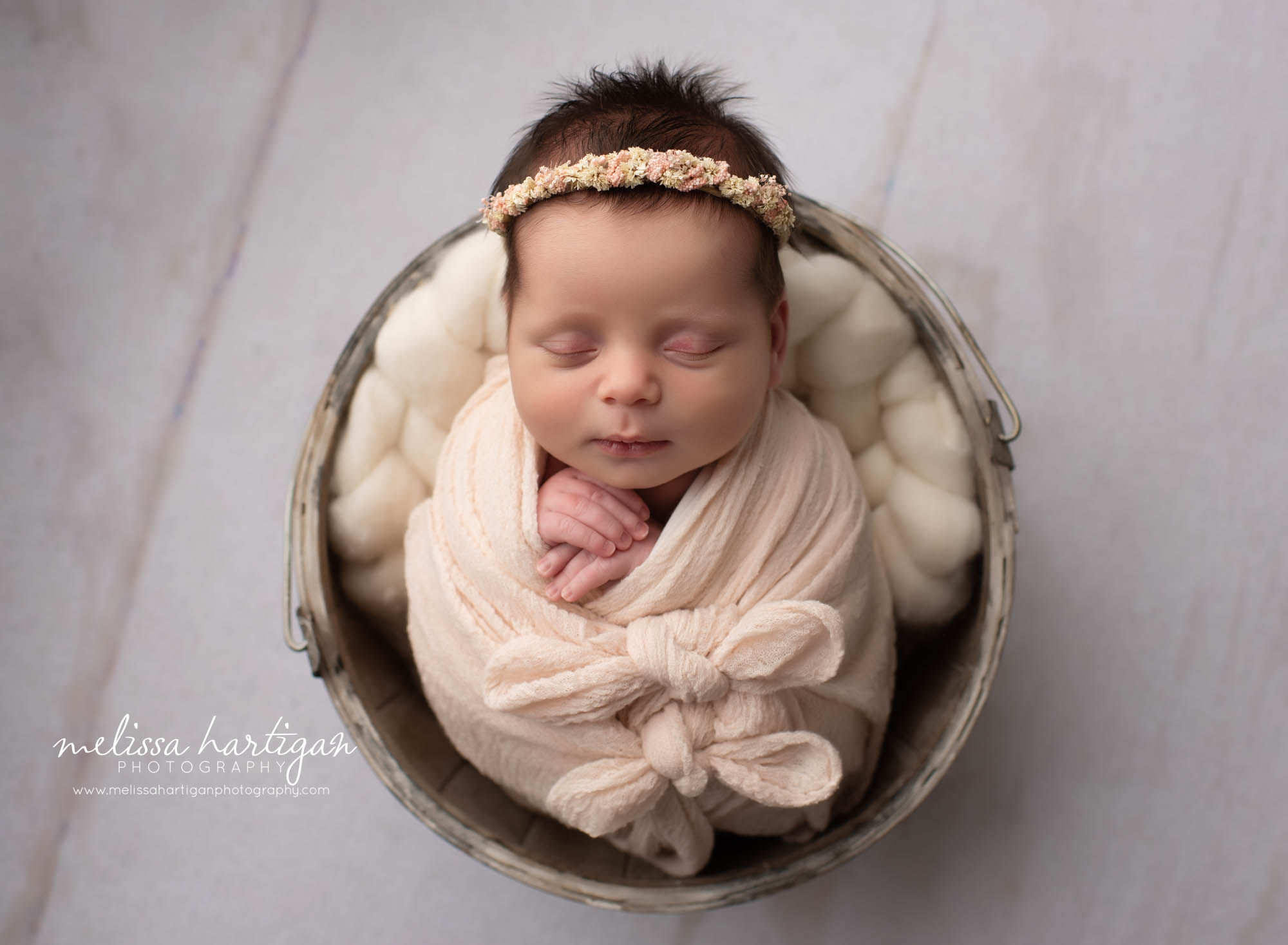 Newborn baby girl wrapped in pink wrap with bows and floral headband