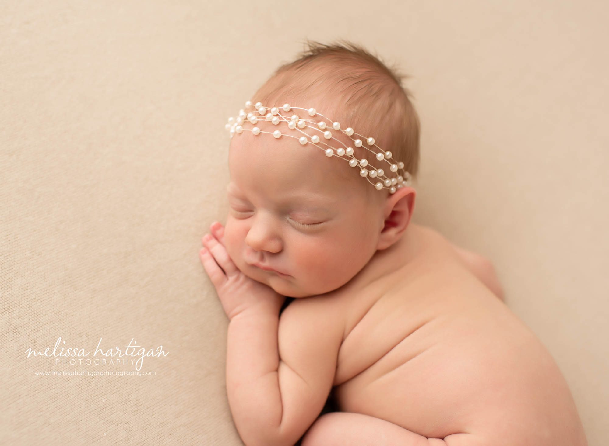 newborn baby girl posed on tummy wearing pearl headband