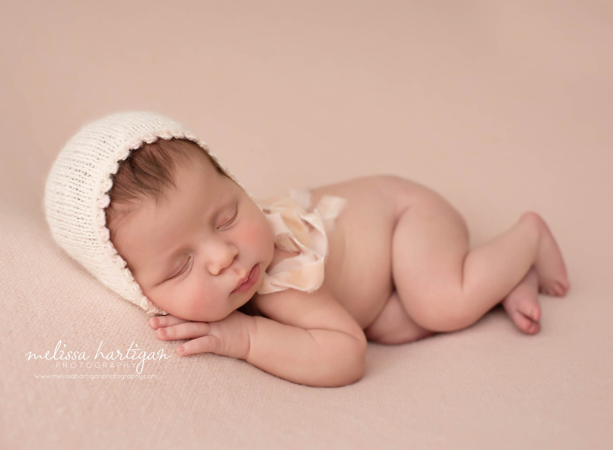 newborn baby girl posed on side wearing cream bonnet