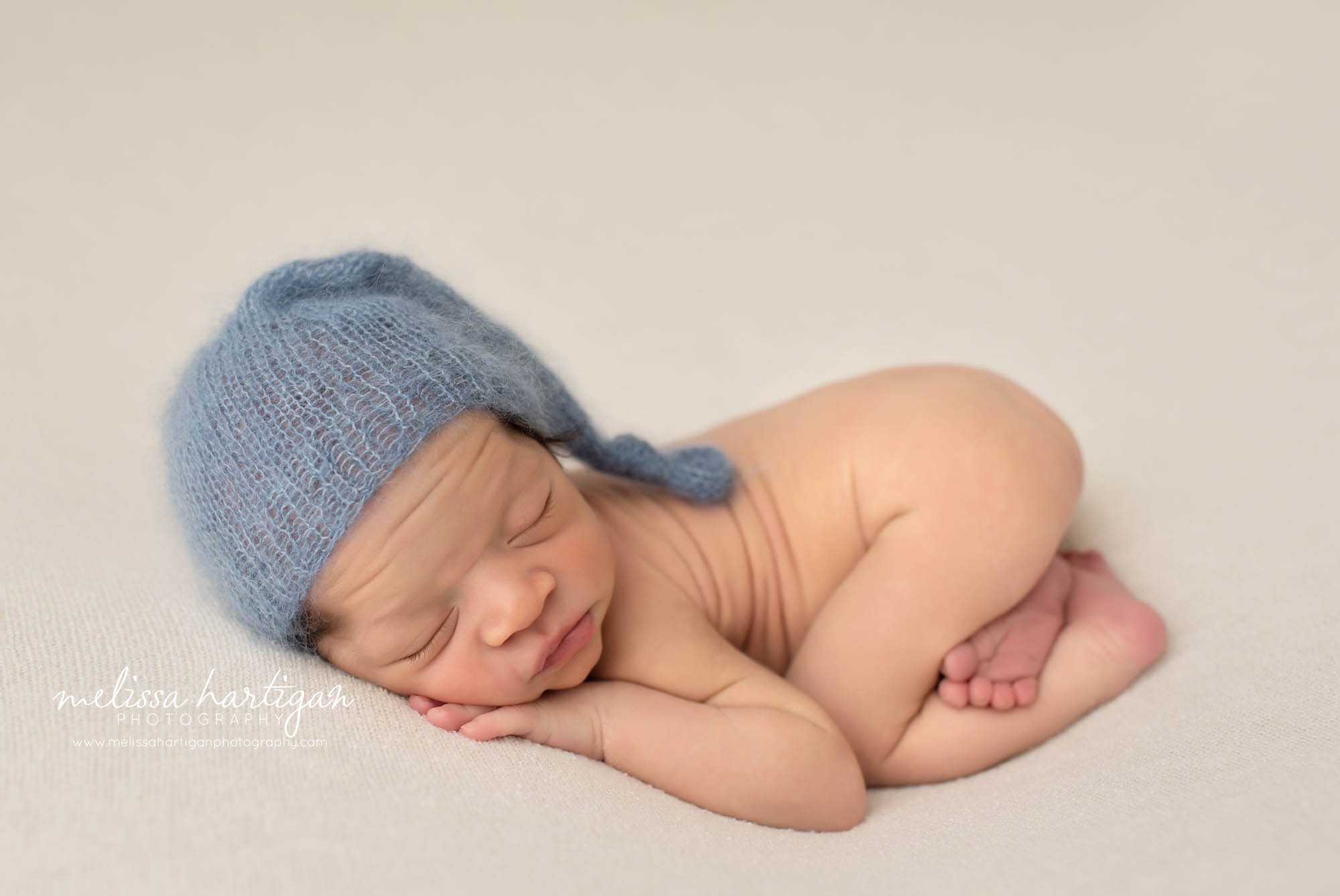 baby boy posed on belyl with bum up wearing blue knitted sleepy cap