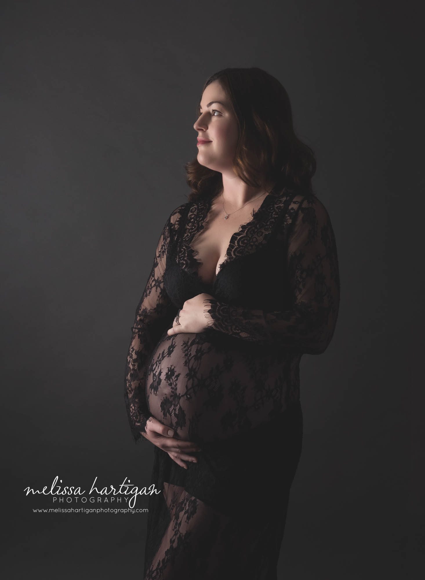 pregnant mom standing against dark background wearing black lace maternity dress Connecticut maternity photographer