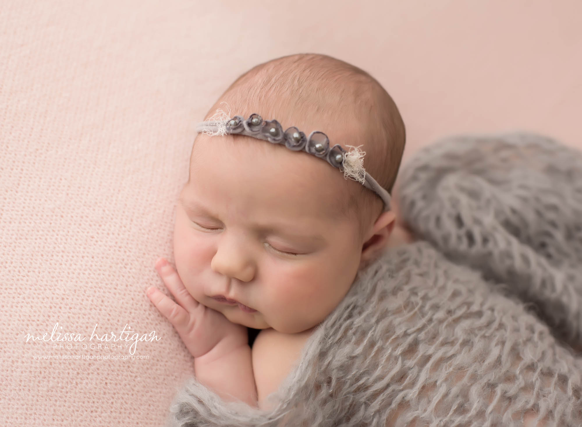 Newborn baby girl posed on side with light gray headband and knitted layer