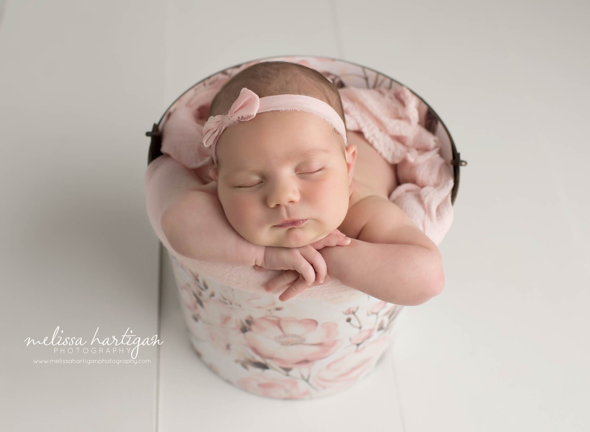 Newborn baby girl posed in floral metal bucket with loigth pink layer and bow headband Coventry Newborn Photography