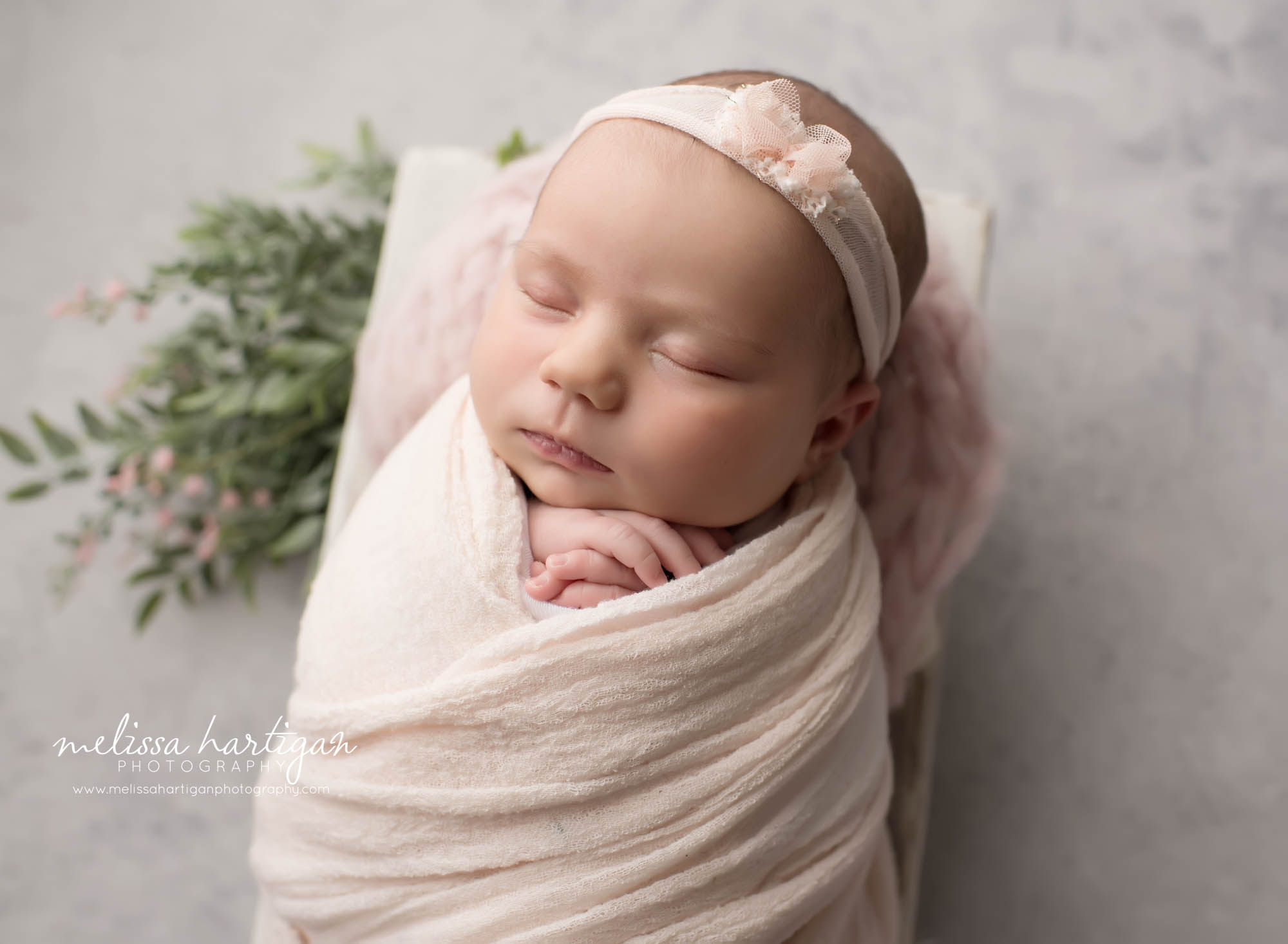 Newborn baby girl wrapped in faint light pink wrap and bow headband