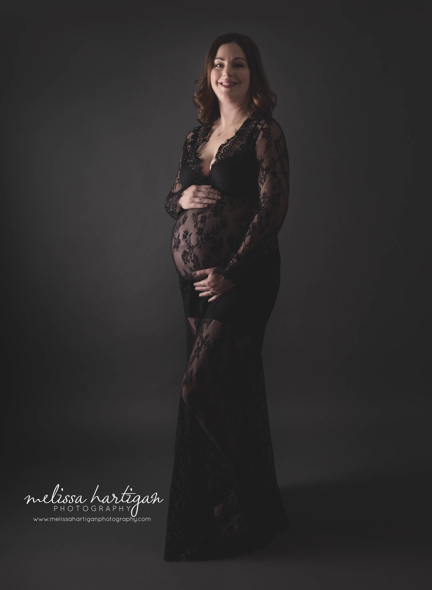 pregnant mom standing against dark background wearing long form fitting black lace maternity dress Maternity photography CT