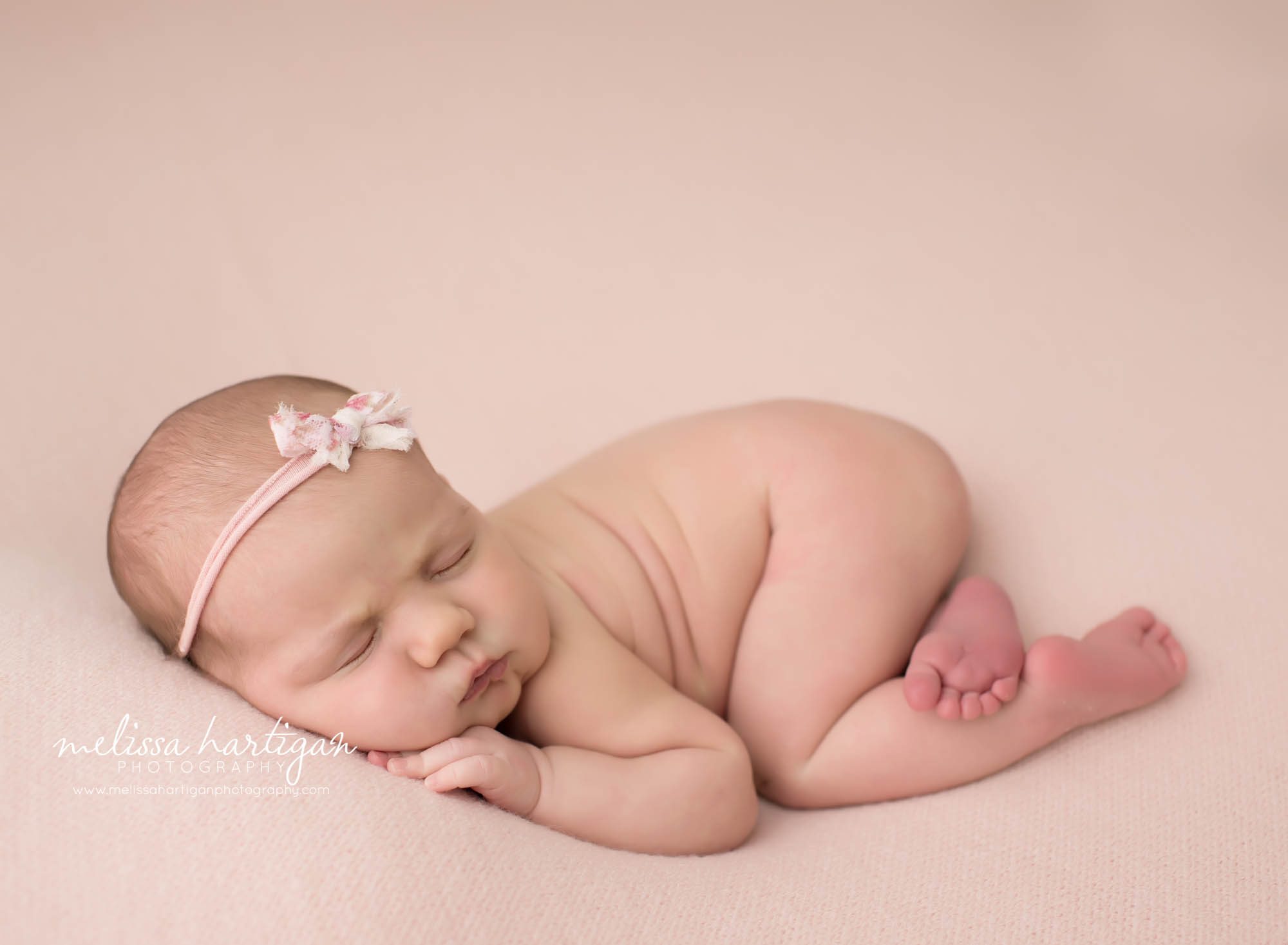 Newborn baby girl posed on side with pink bow