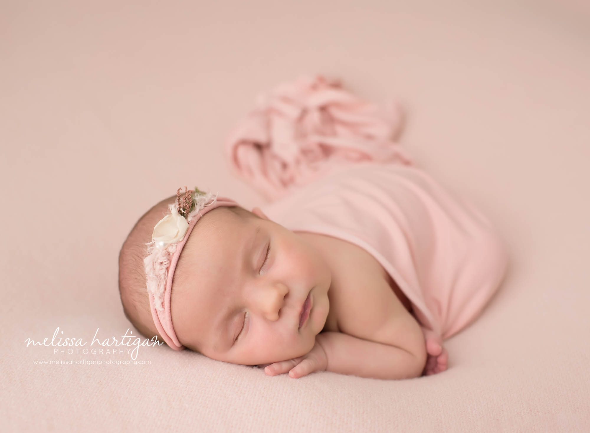 newborn baby girl posed on side with flower headband and pink layer draped over newborn photography coventry